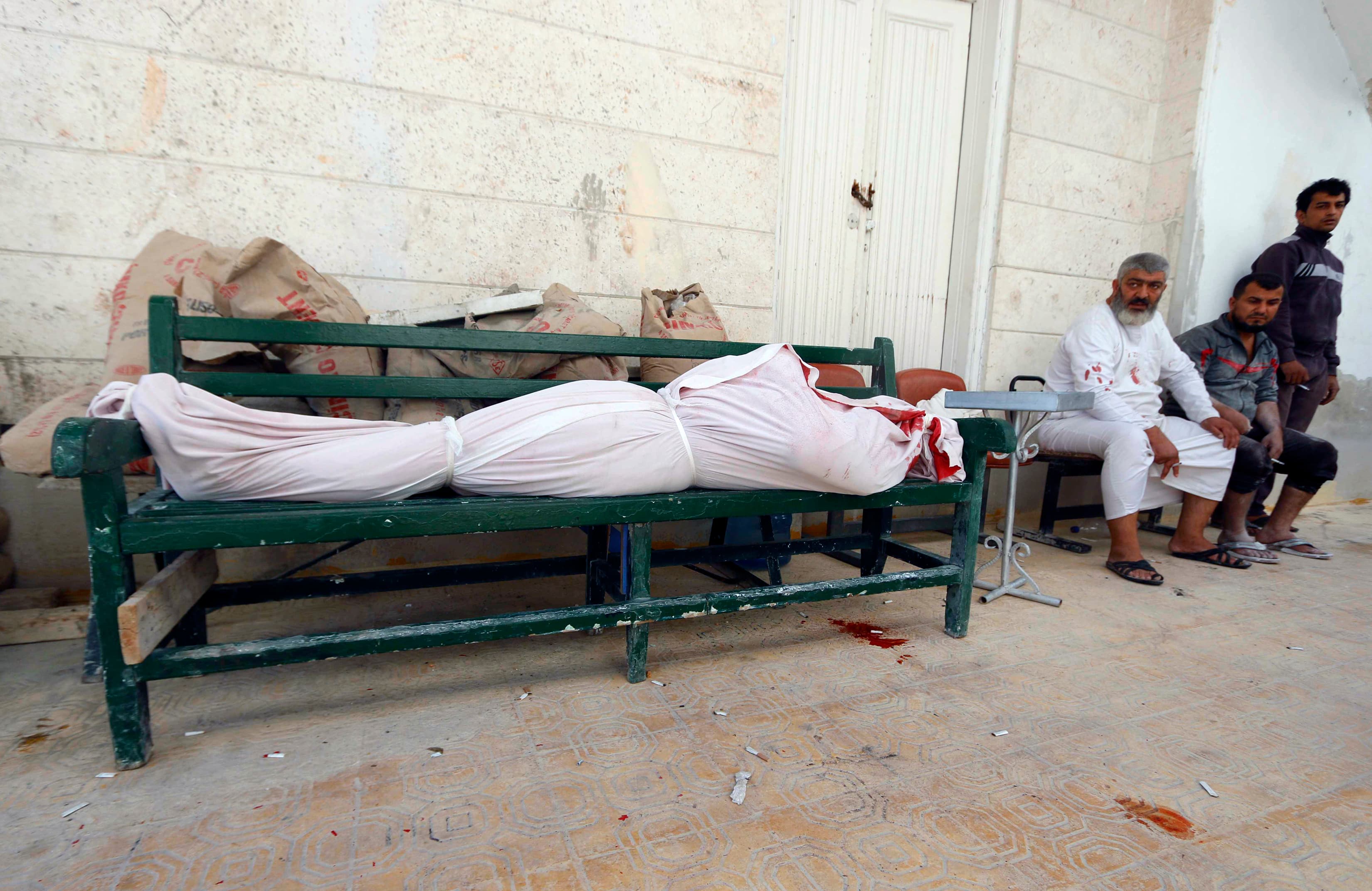 Men sit near a dead body wrapped in white after what activists said was a barrel bomb was dropped by forces loyal to Syrian President Bashar al-Assad in Aleppo on October 1, 2014.