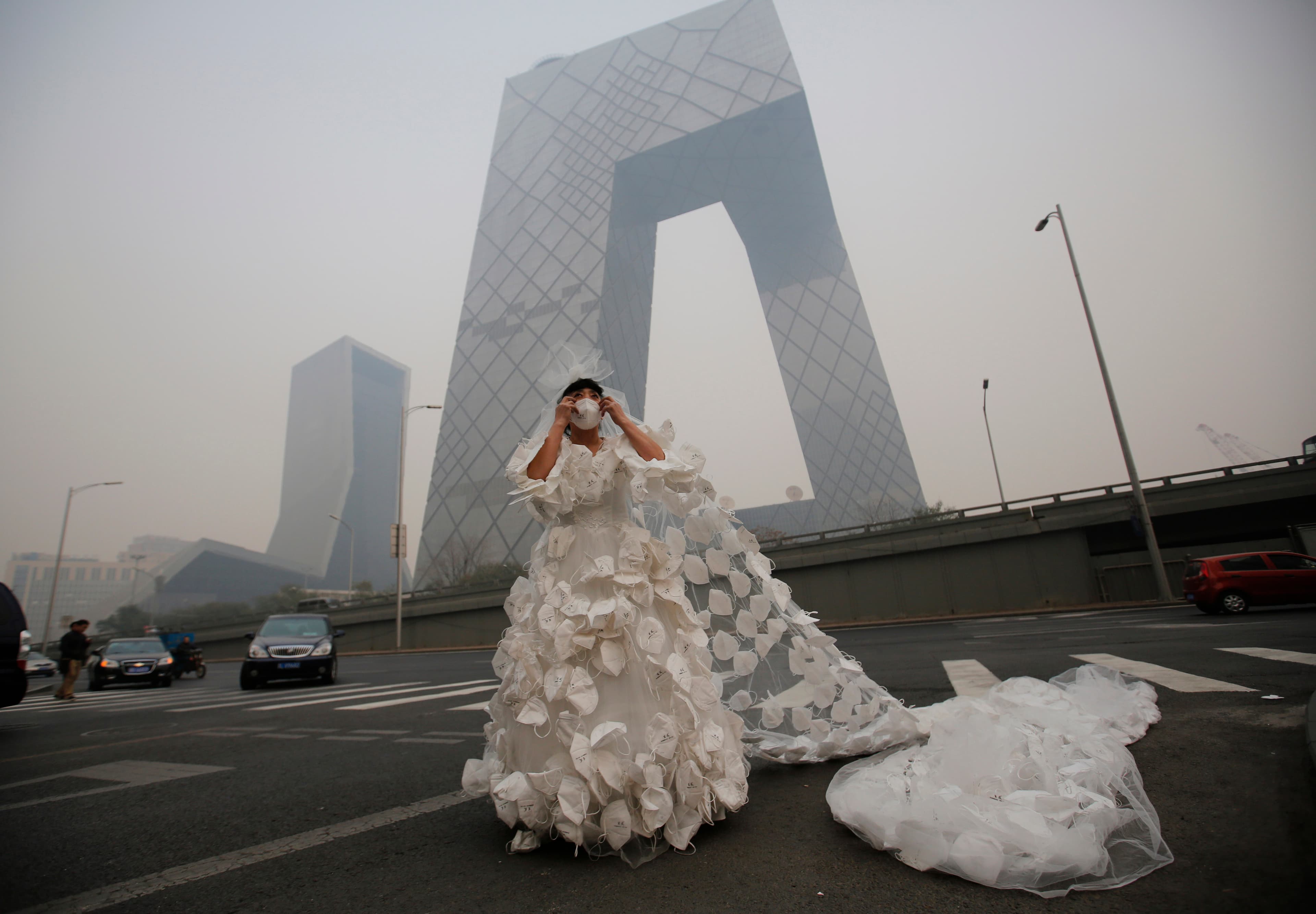 Kong Ning wears a wedding dress decorated with 999 face masks for her performance art work 'Marry the blue sky' as she poses for a photograph in front of the China Central Television (CCTV) Headquarters on a hazy day in Beijing November 19, 2014.