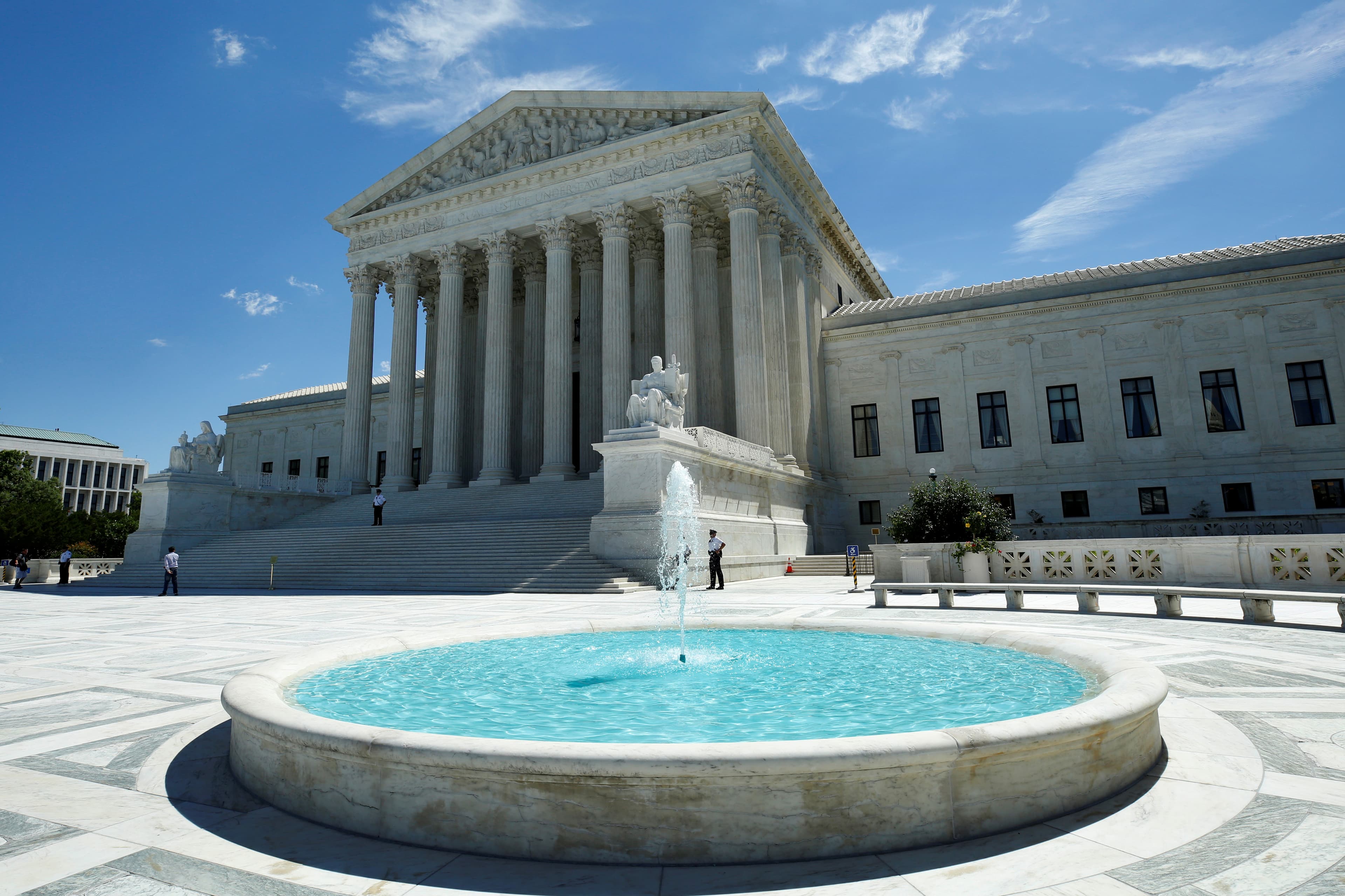 View of white building with columns from behind blue, still water fountain