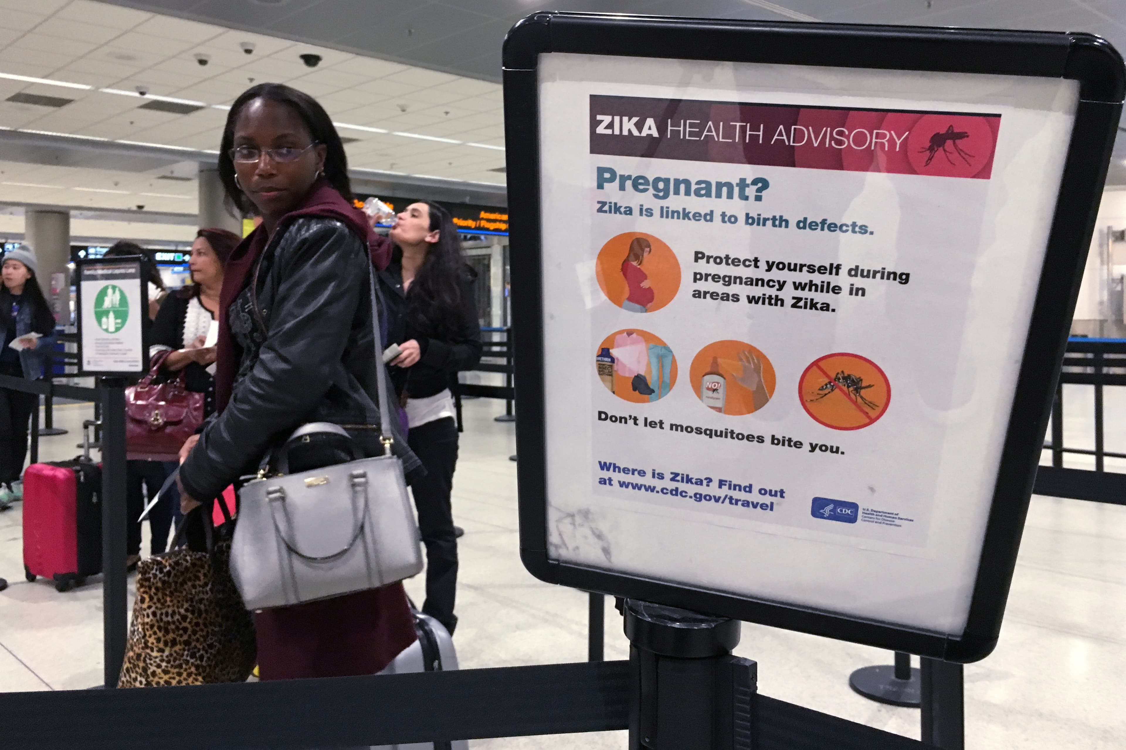 A woman looks at a Center for Disease Control (CDC) health advisory sign about the dangers of the Zika virus as she lines up for a security screening at Miami International Airport in Miami, Florida, U.S., May 23, 2016.