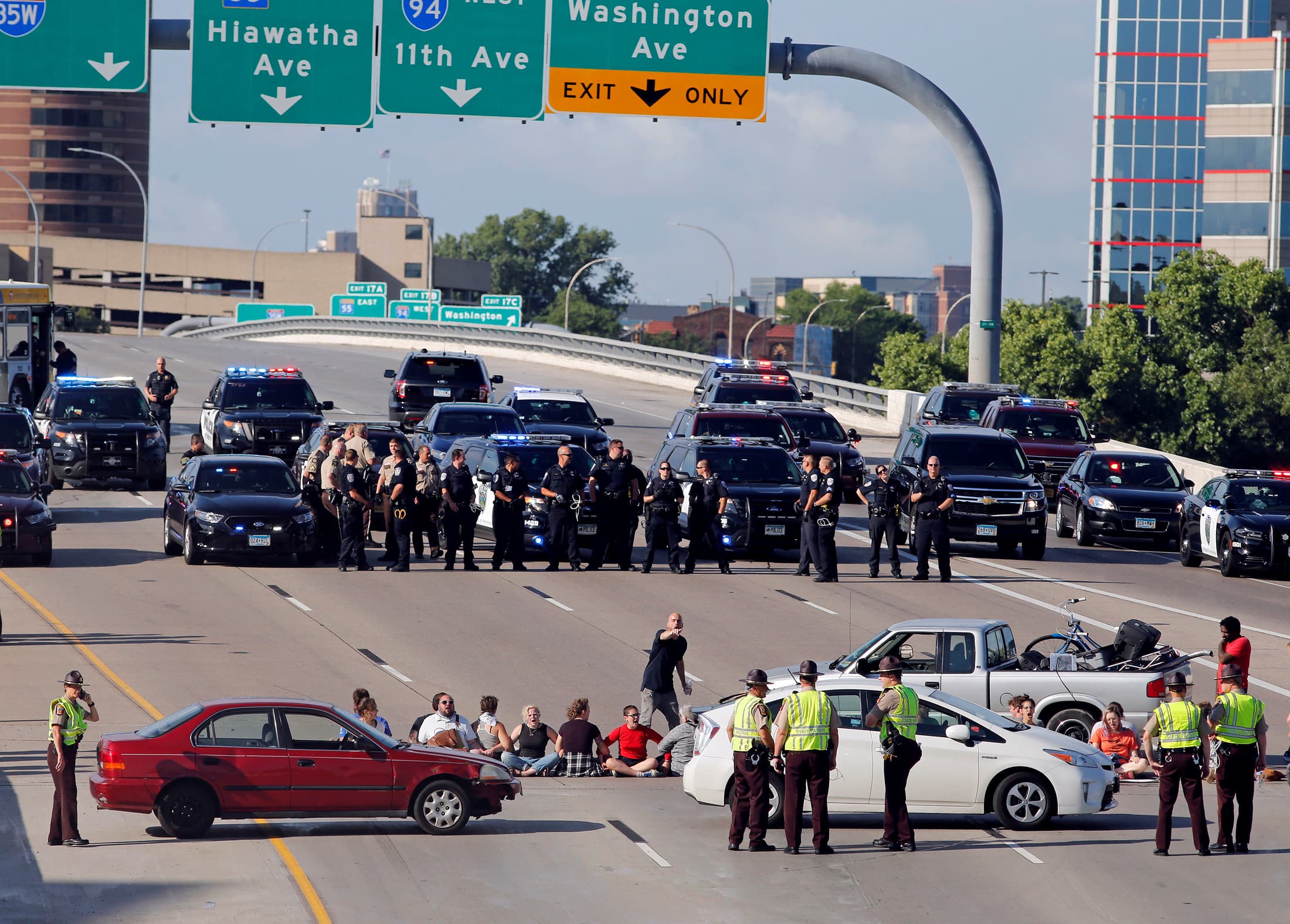 An aerial view of freeway, with rows of police and protesters in front of an off-ramp