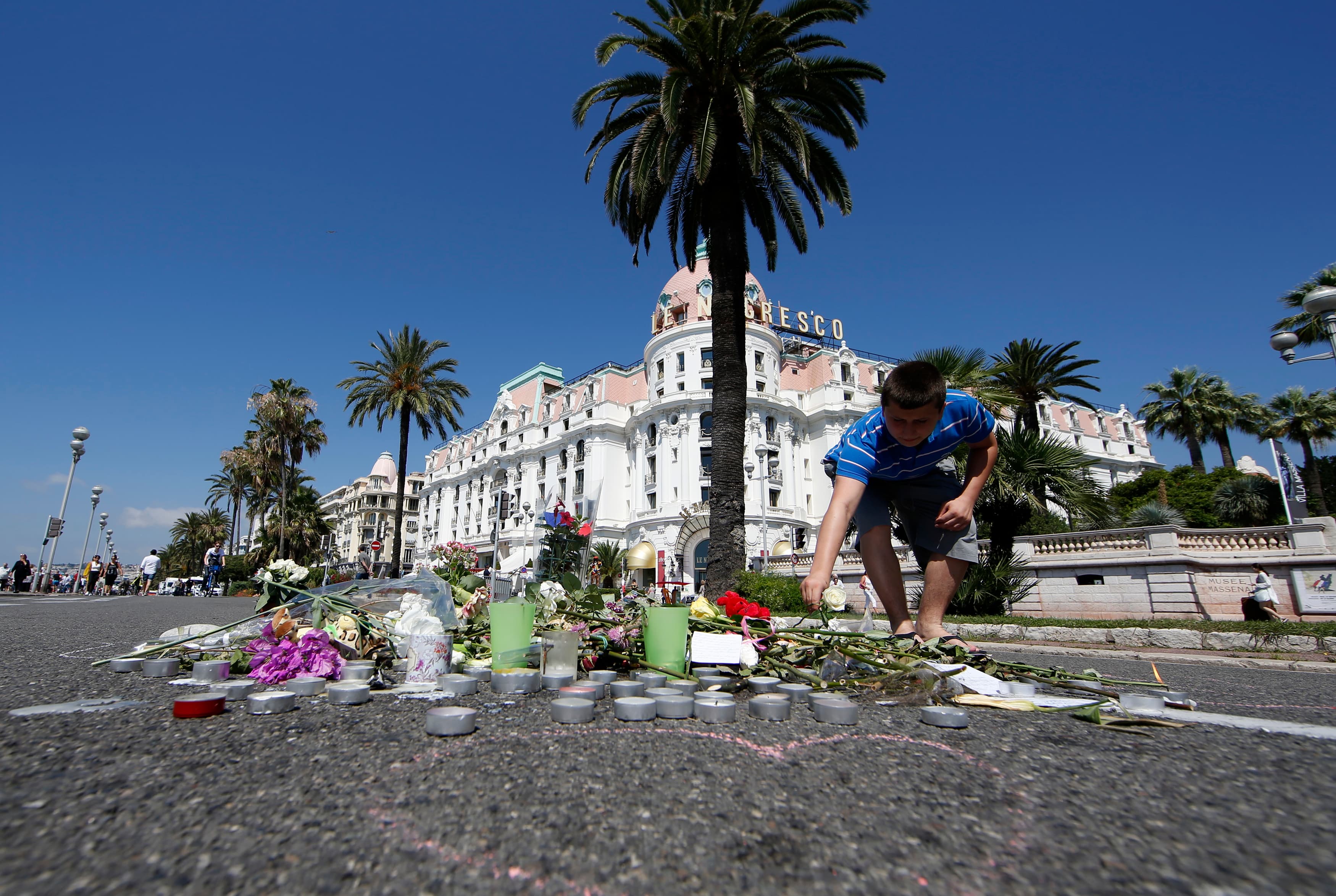 A boy places a white rose on the road in front of the Negresco hotel before a minute of silence on the third day of national mourning to pay tribute to victims of the truck attack along the Promenade des Anglais.