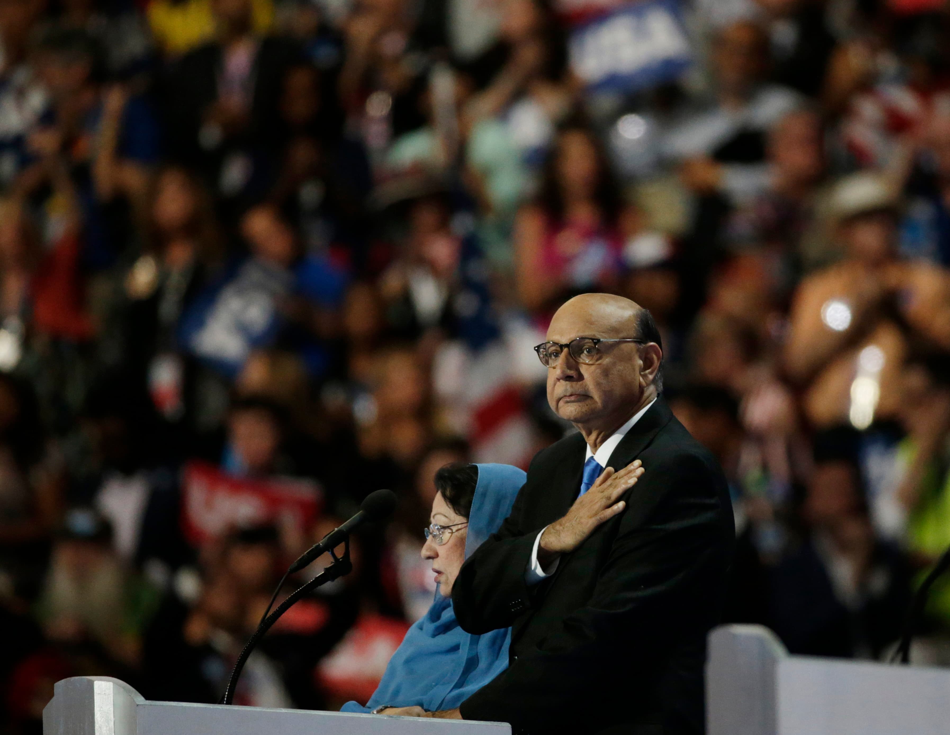 Man in front of crowd holds hand to heart, with woman standing next to him