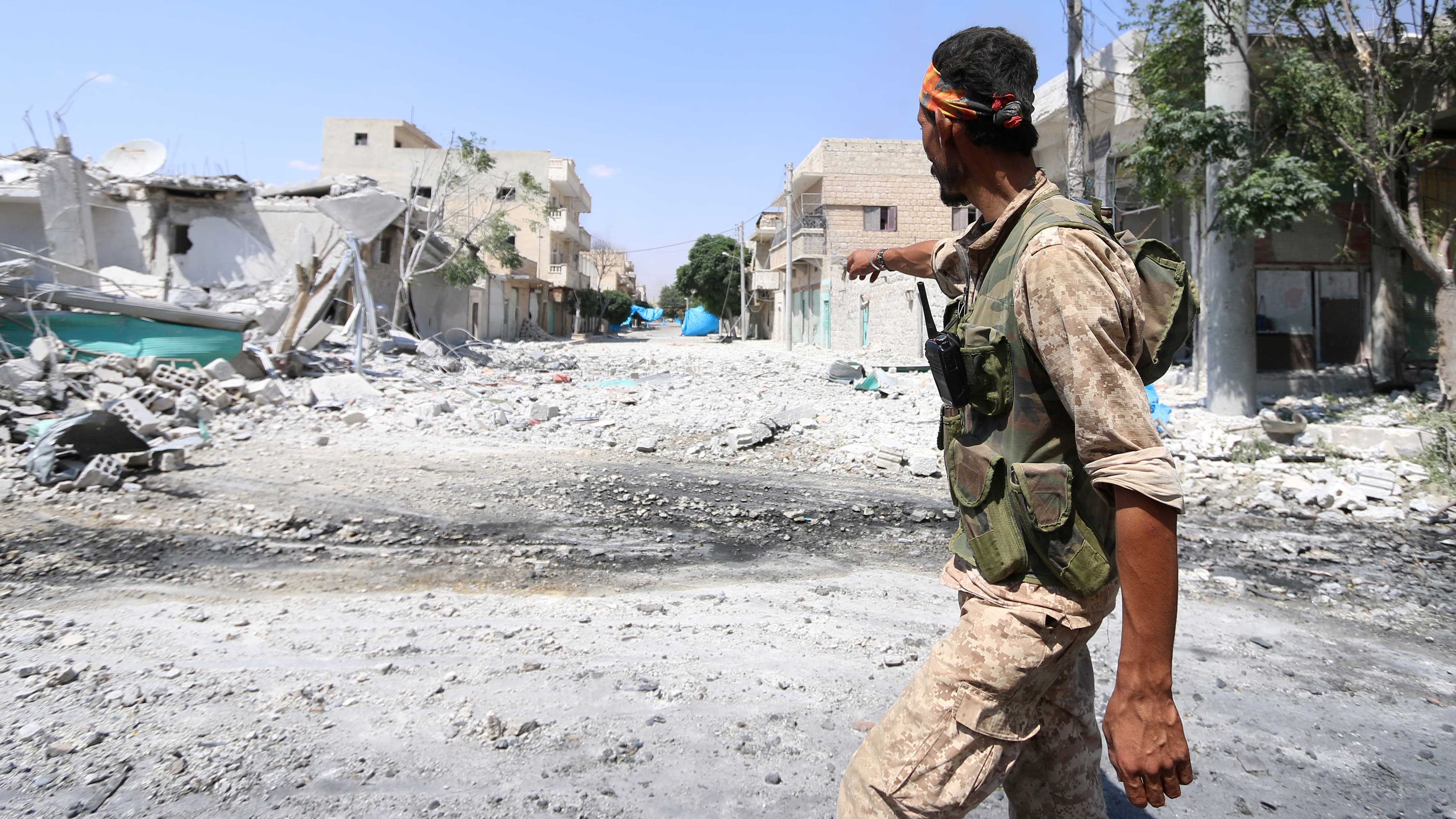 A Syria Democratic Forces (SDF) fighter points towards blue sheets spread over streets as a cover from snipers as he walks on the rubble of damaged buildings in Manbij, in Aleppo Governorate, Syria, August 7, 2016.