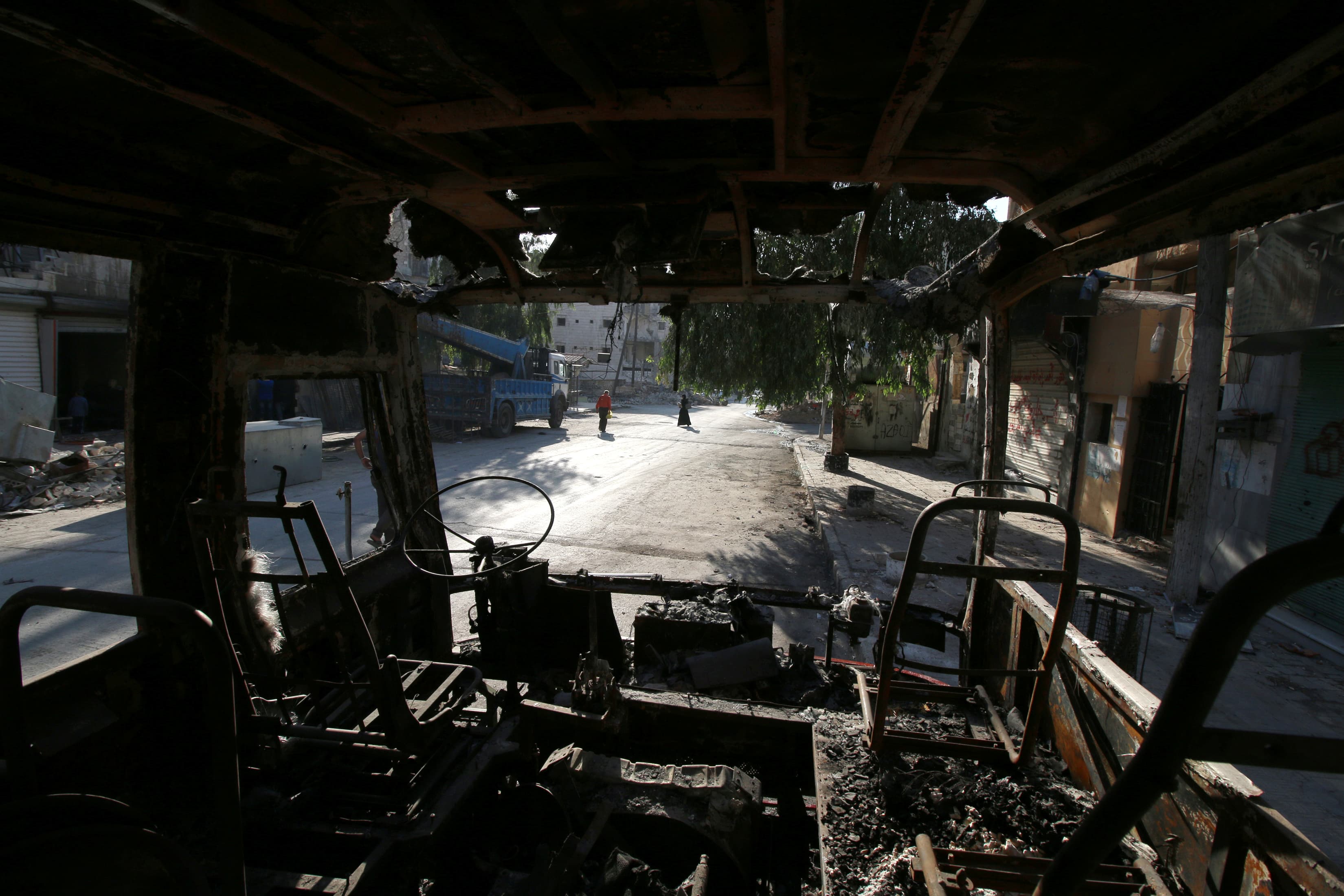 Aleppo residents walk past a burnt bus in the city's rebel-held Seif al-Dawla neighborhood.