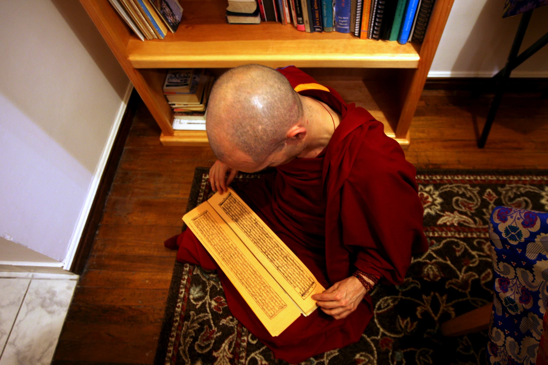 A Tibetan Buddhist monk reads from a traditional Tibetan book sitting in his lap.