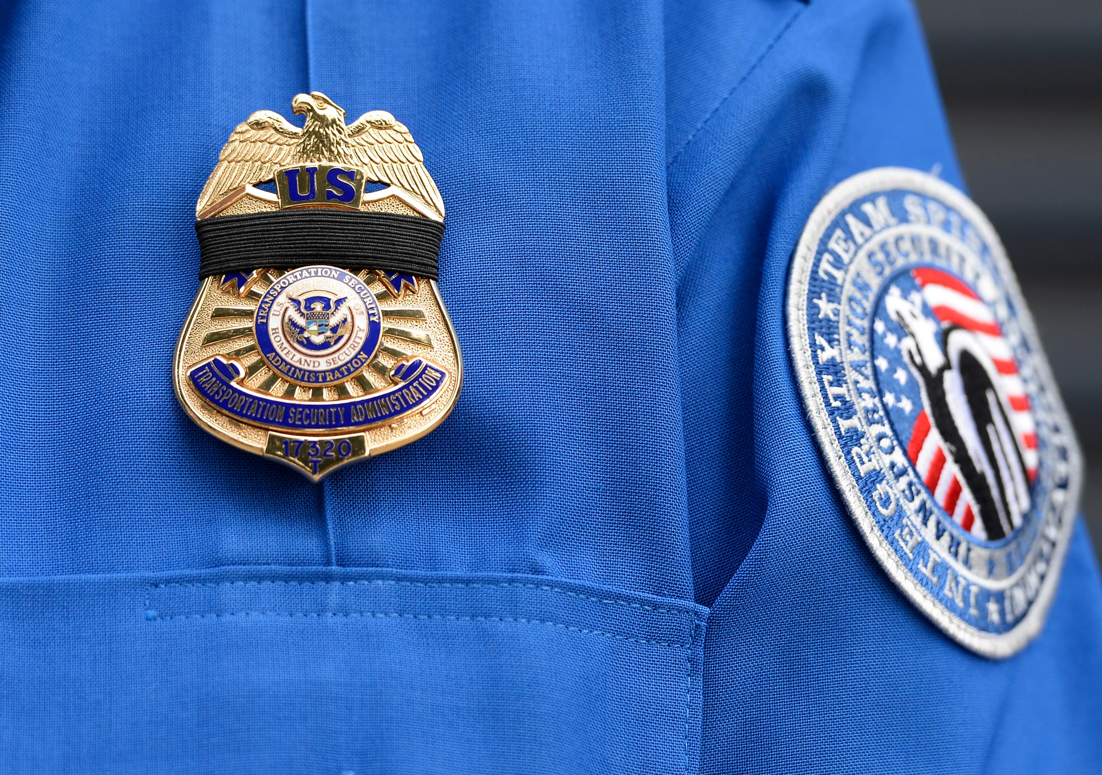 A TSA agent wears a black ribbon over his badge during a memorial service for a slain colleague.