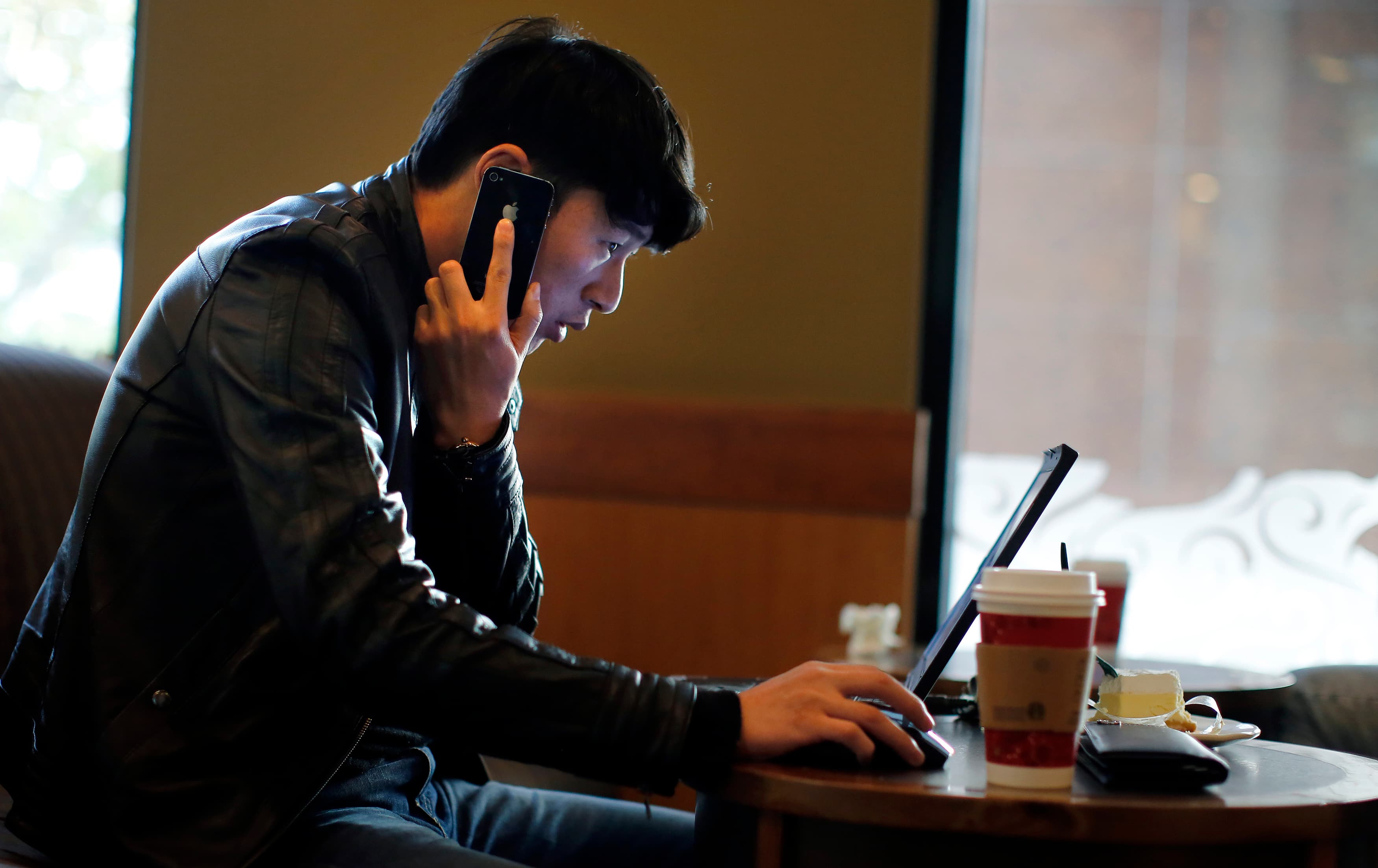 A man talks on the phone as he surfs the internet on his laptop at a local coffee shop in downtown Shanghai.