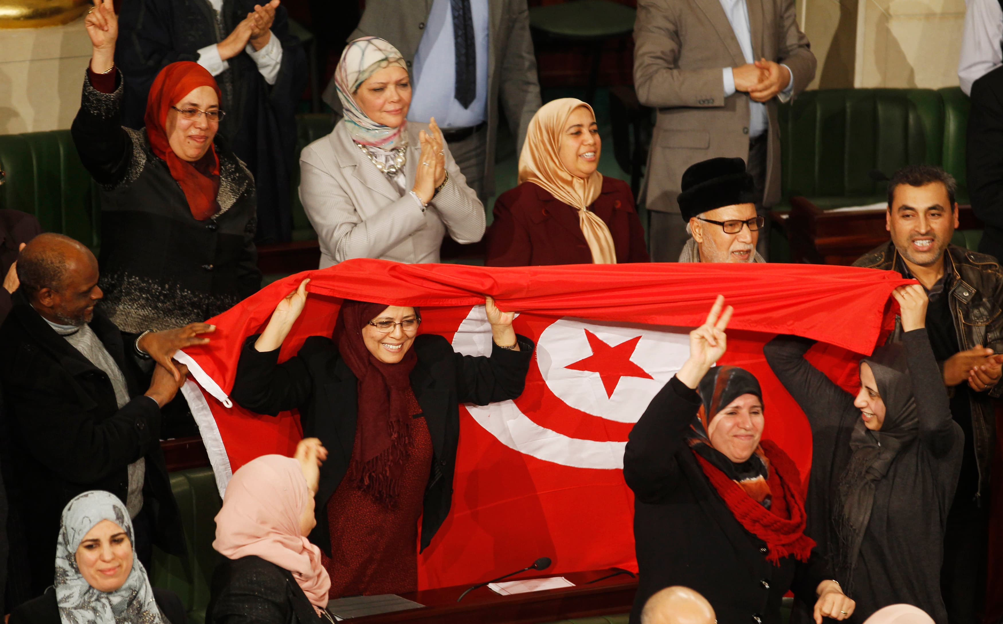 Members of the Tunisian parliament wave flags after approving the country's new constitution.. Tunisia's national assembly approved the country's new constitution on Sunday in one of the final steps to full democracy three years after protests erupted int