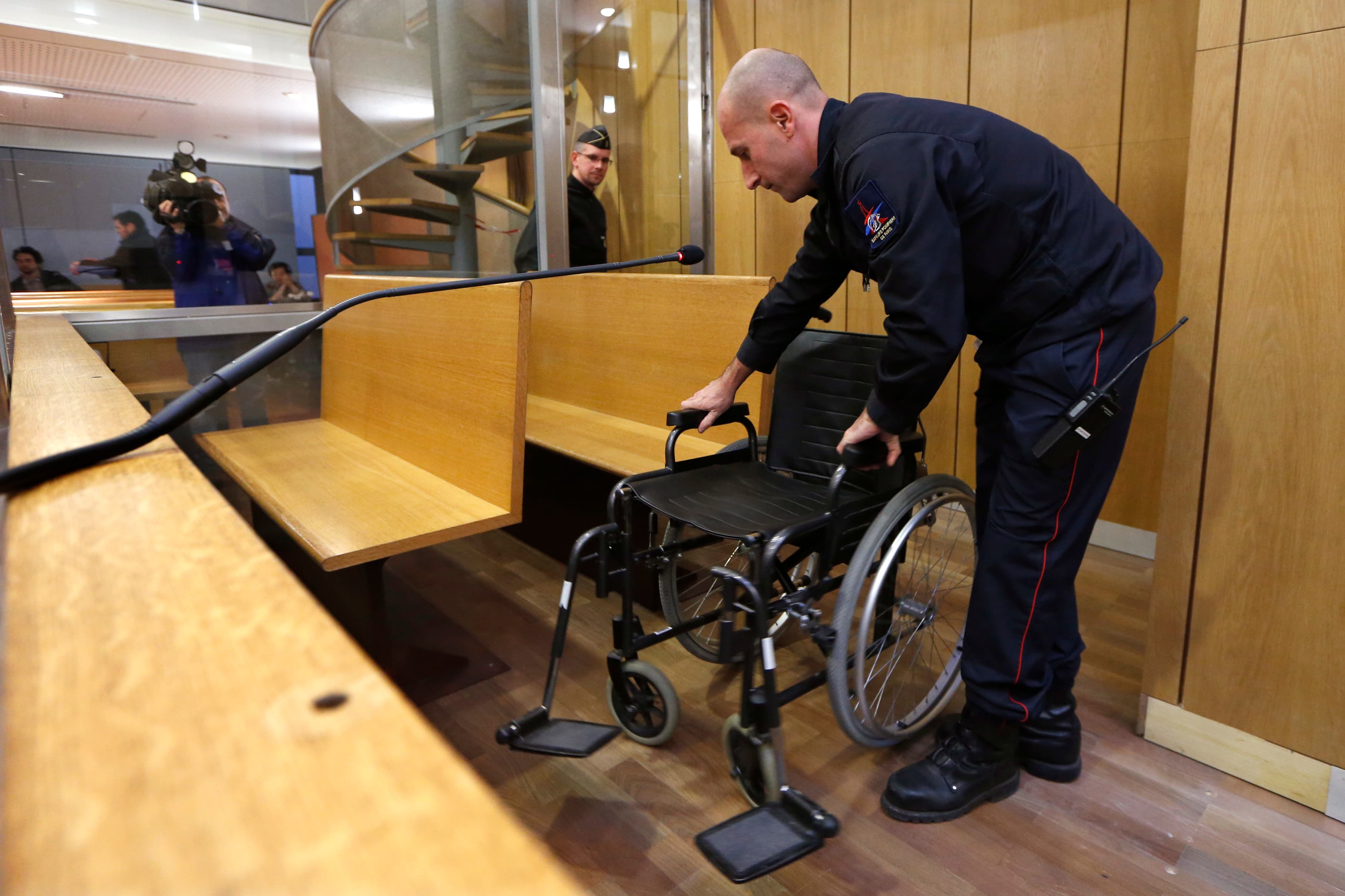 A fireman installs the wheelchair of former Rwandan army captain Pascal Simbikangwa before the start of his trial at a Paris court.