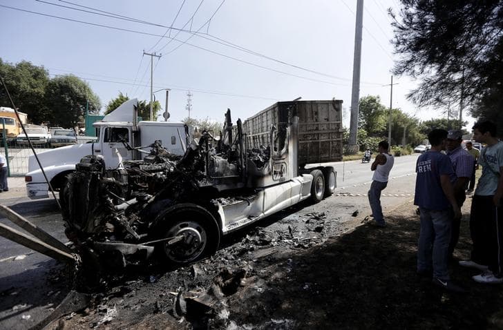 Men stand next to the wreckage of a tractor-trailer set ablaze by members of a drug cartel in Guadalajara May 1, 2015.
