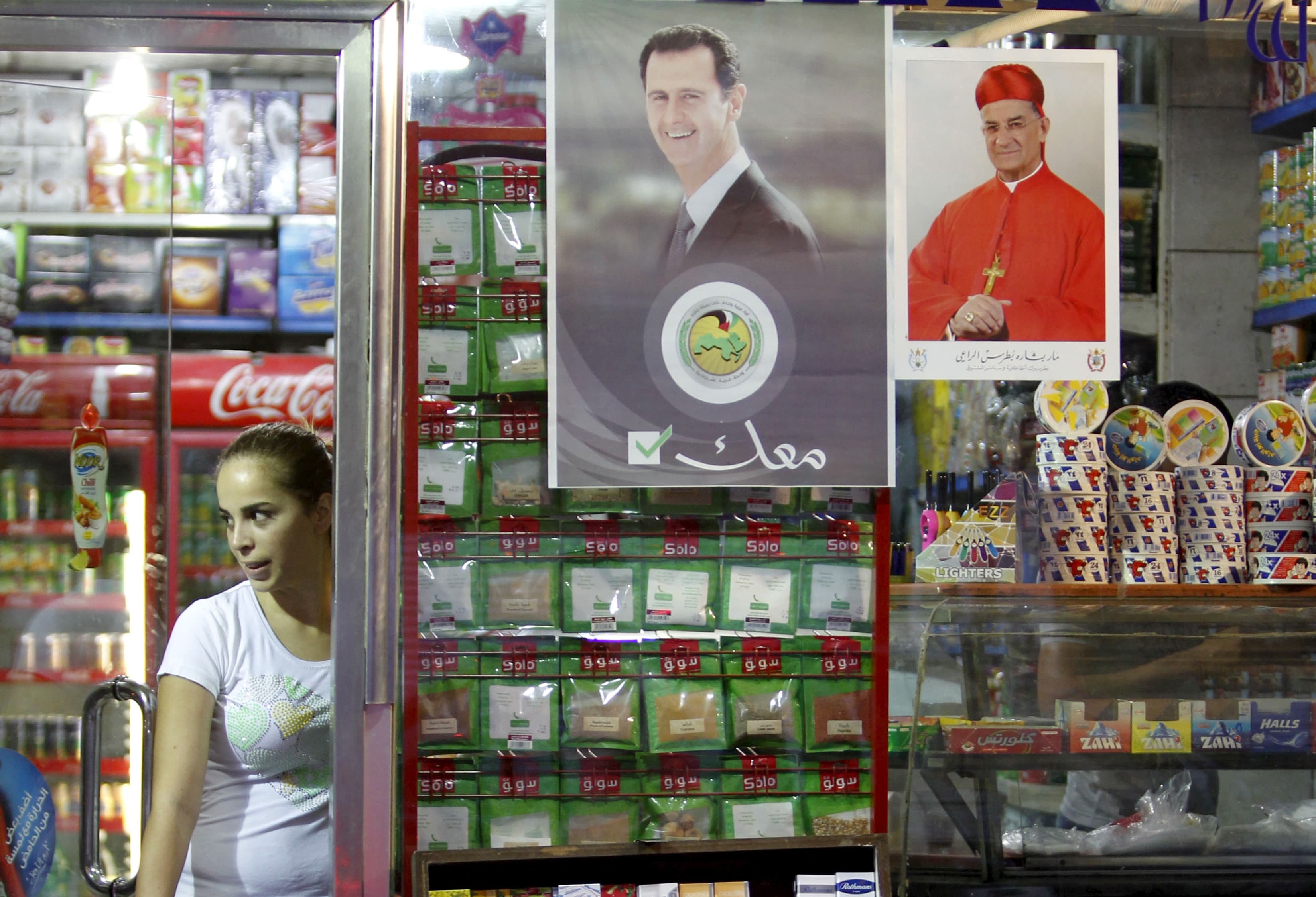 A woman stands inside a Damascus grocery shop beside a picture of Syria's President Bashar al-Assad. The text beneath the Syrian leader reads "With you" in Arabic.