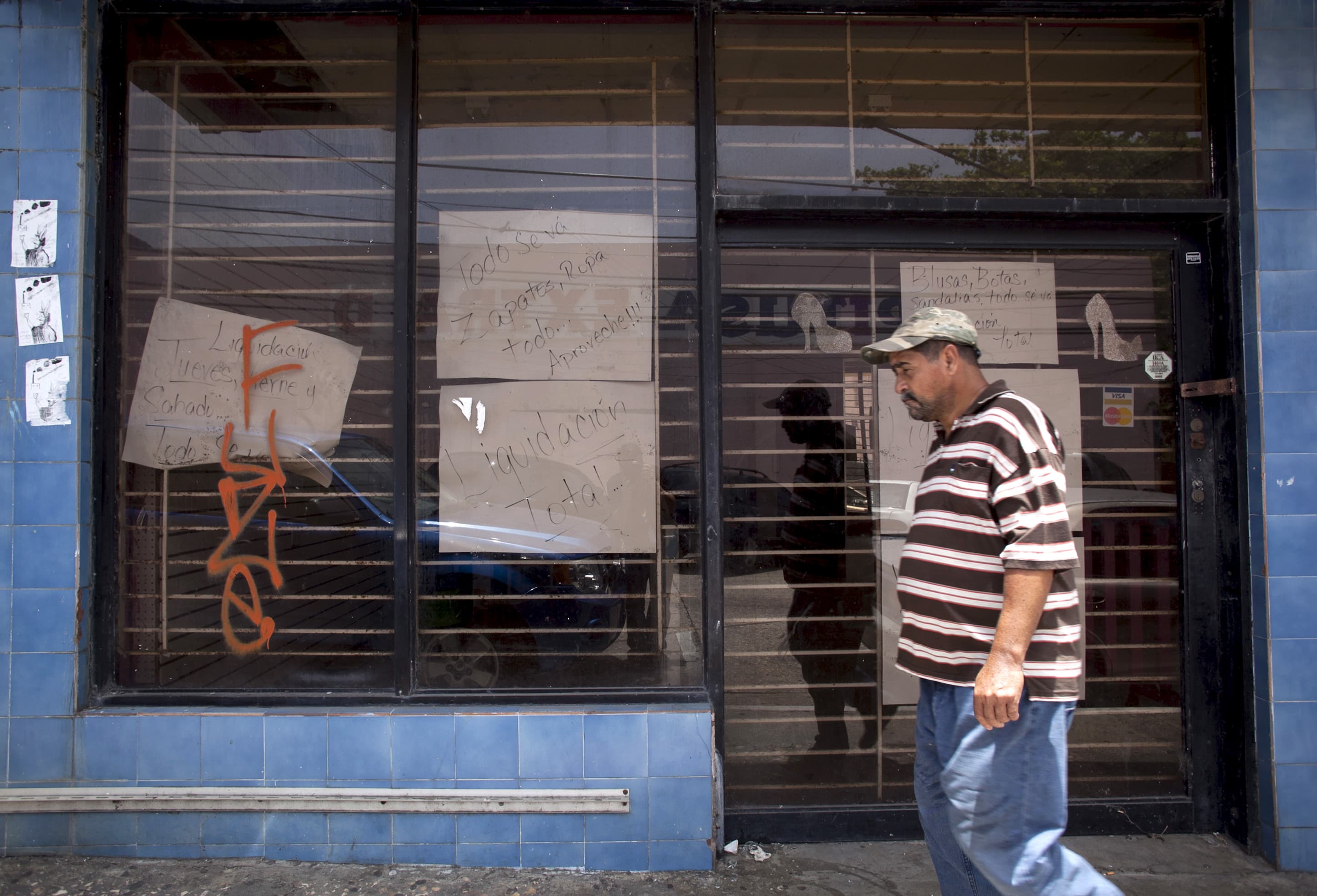 A man walks past a closed store with signs reading "Closing down sale" and "Everything goes, shoes, clothes, take advantage" in Arecibo, Puerto Rico, June 29, 2015.
