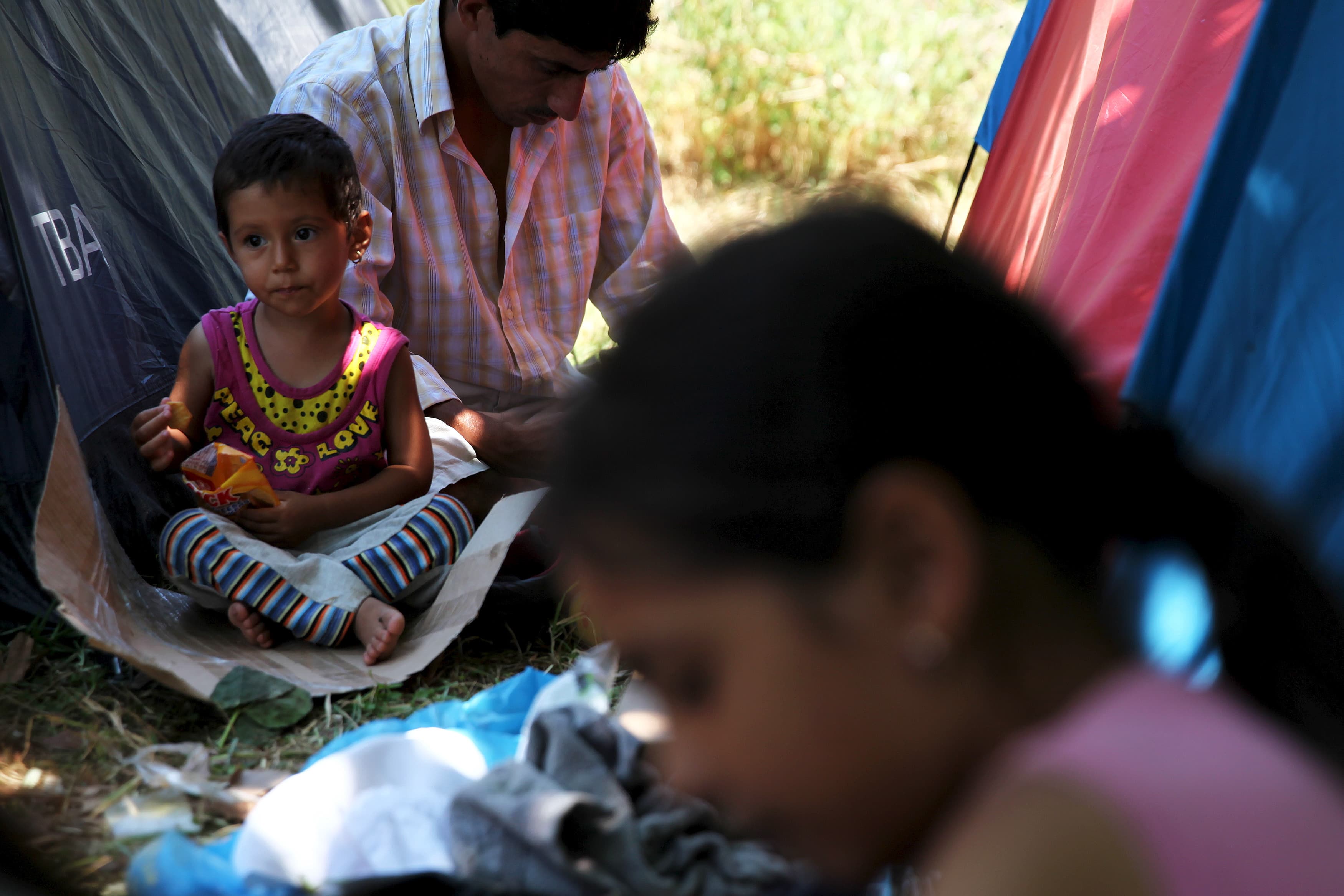 A child (L) eats crackers at a migrants make-shift camp in a park in central Athens, Greece July 24, 2015.