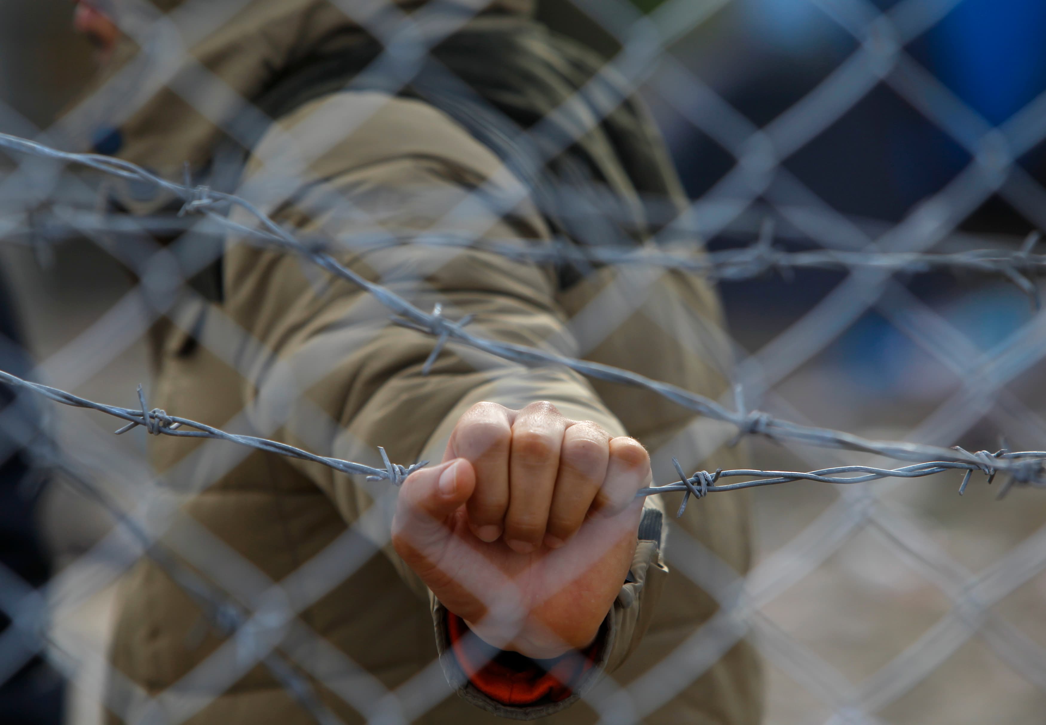 A migrant holds a barbed wire fence at the Macedonian-Greek border, near Gevgelija, Macedonia, November 29, 2015.