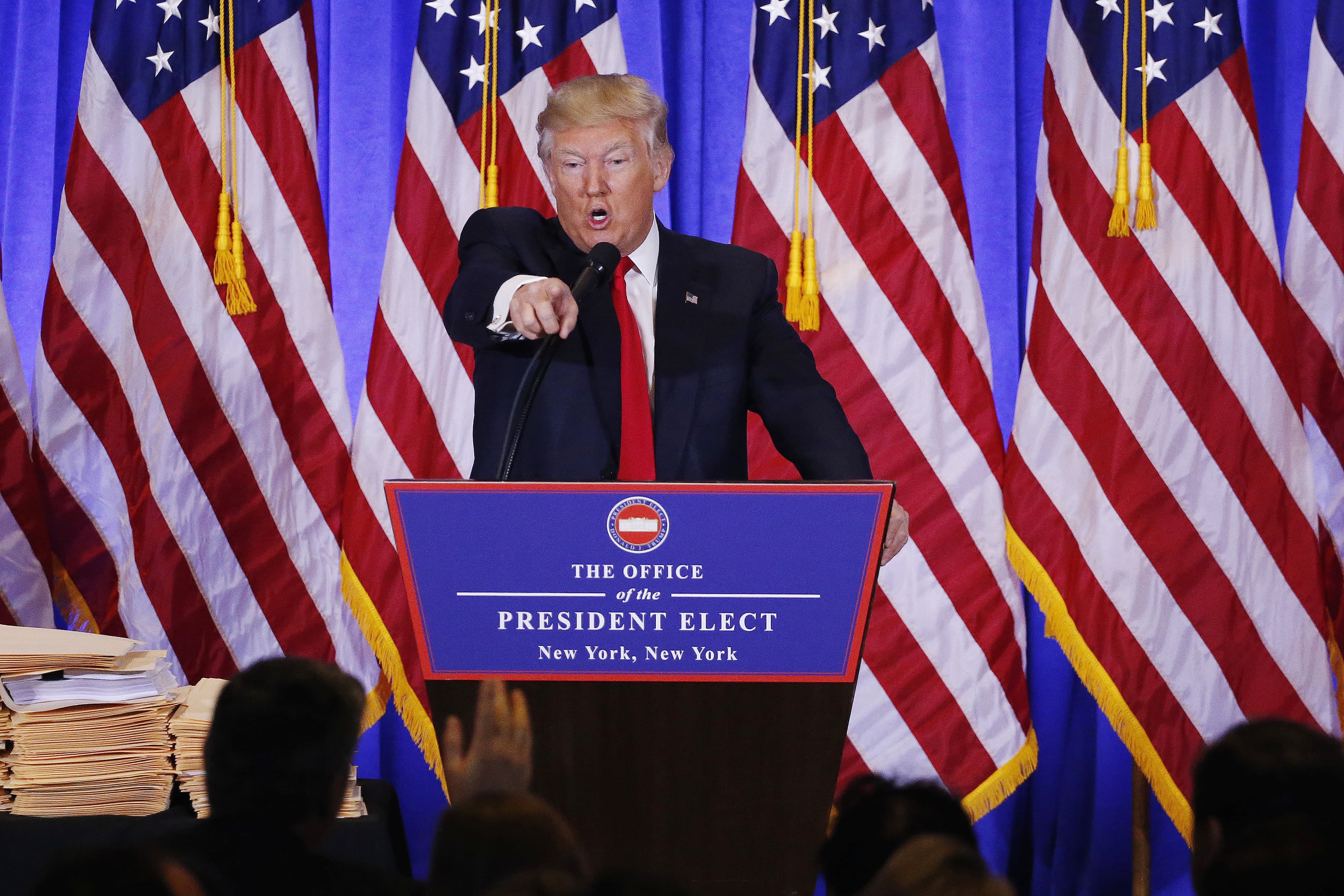 Trump pointing over podium, with flags behind him