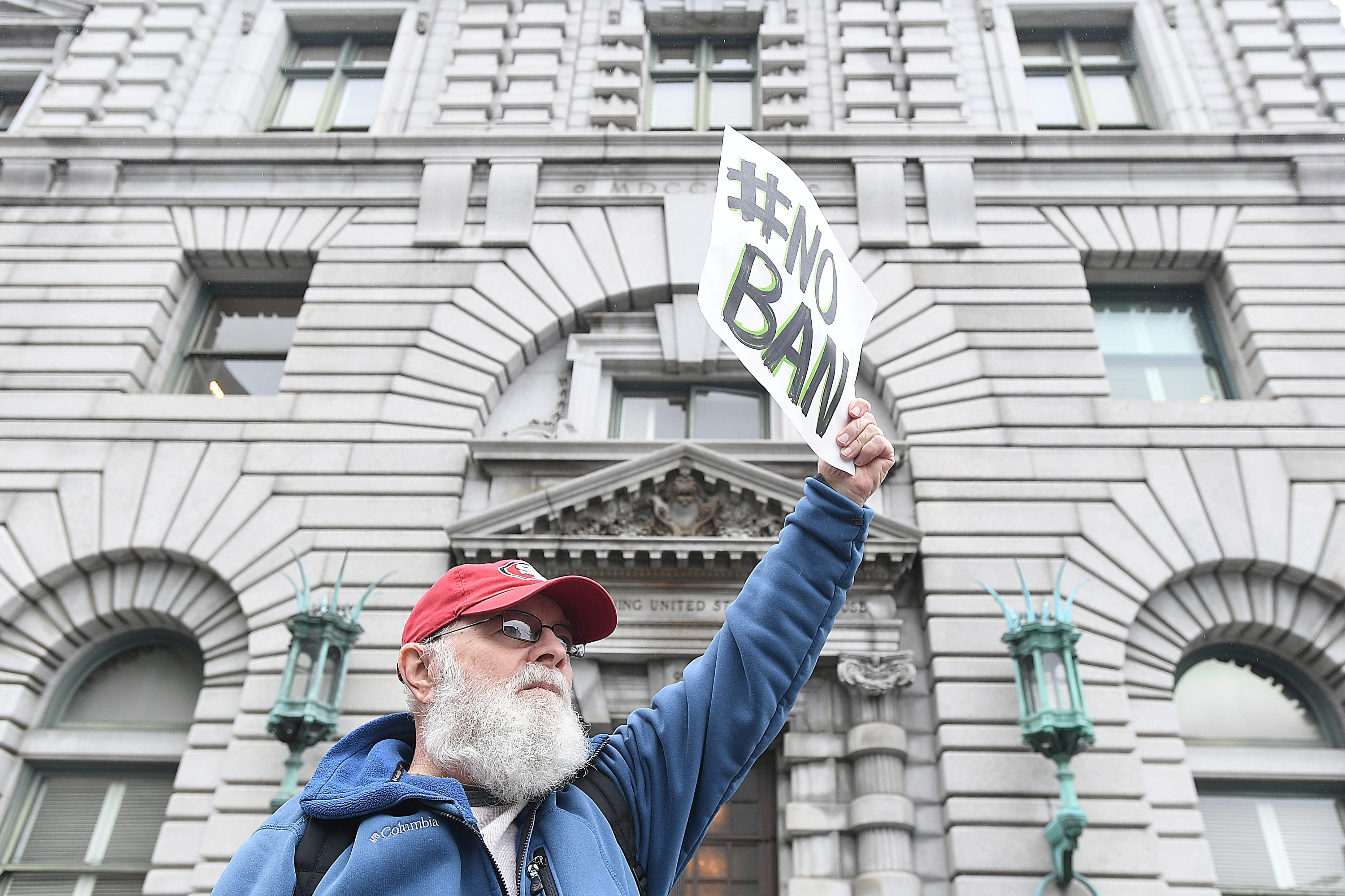 Man in front of courthouse with #NoBan sign