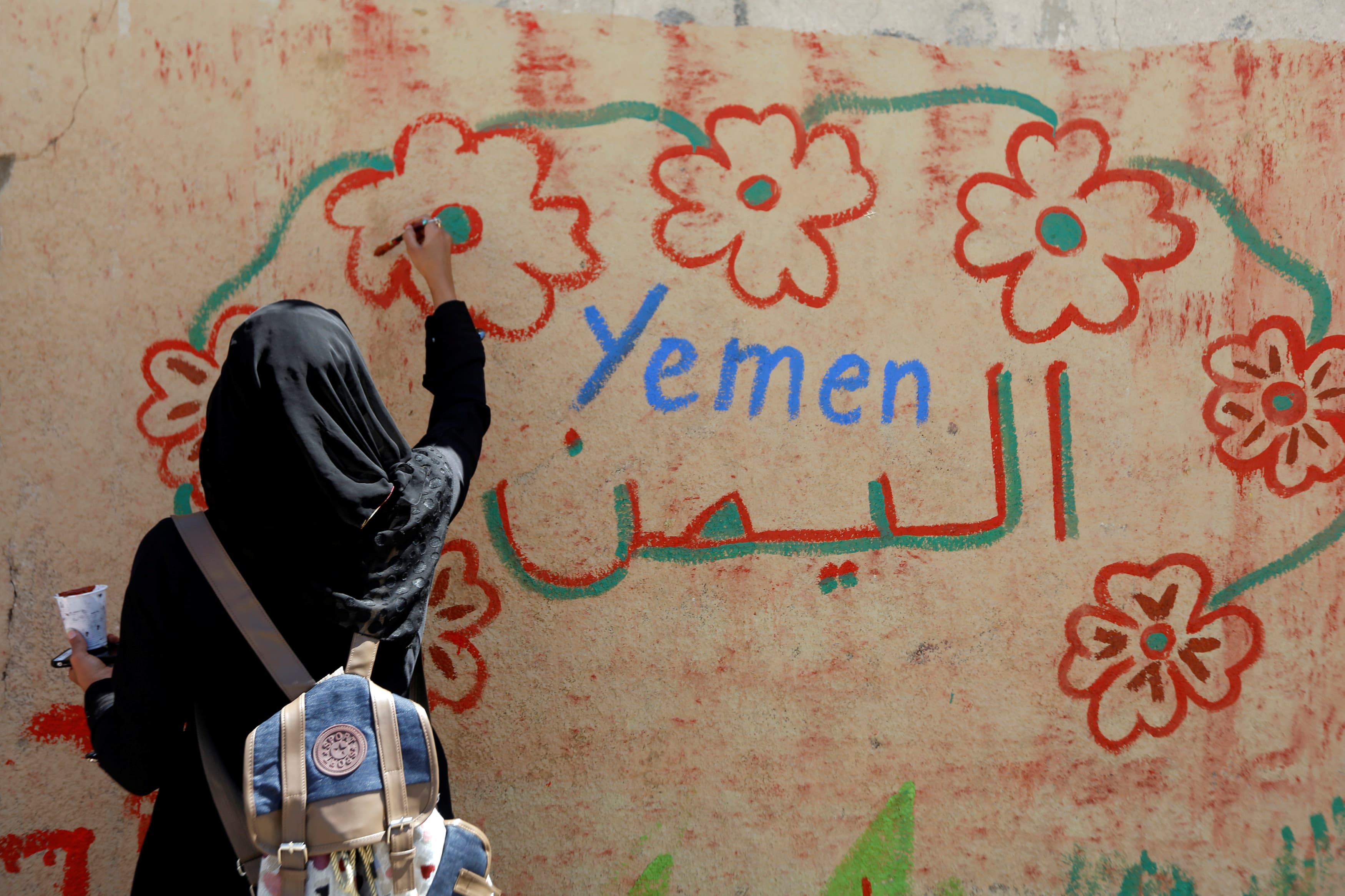 A woman takes part in a graffiti painting campaign on a wall in Sanaa, Yemen