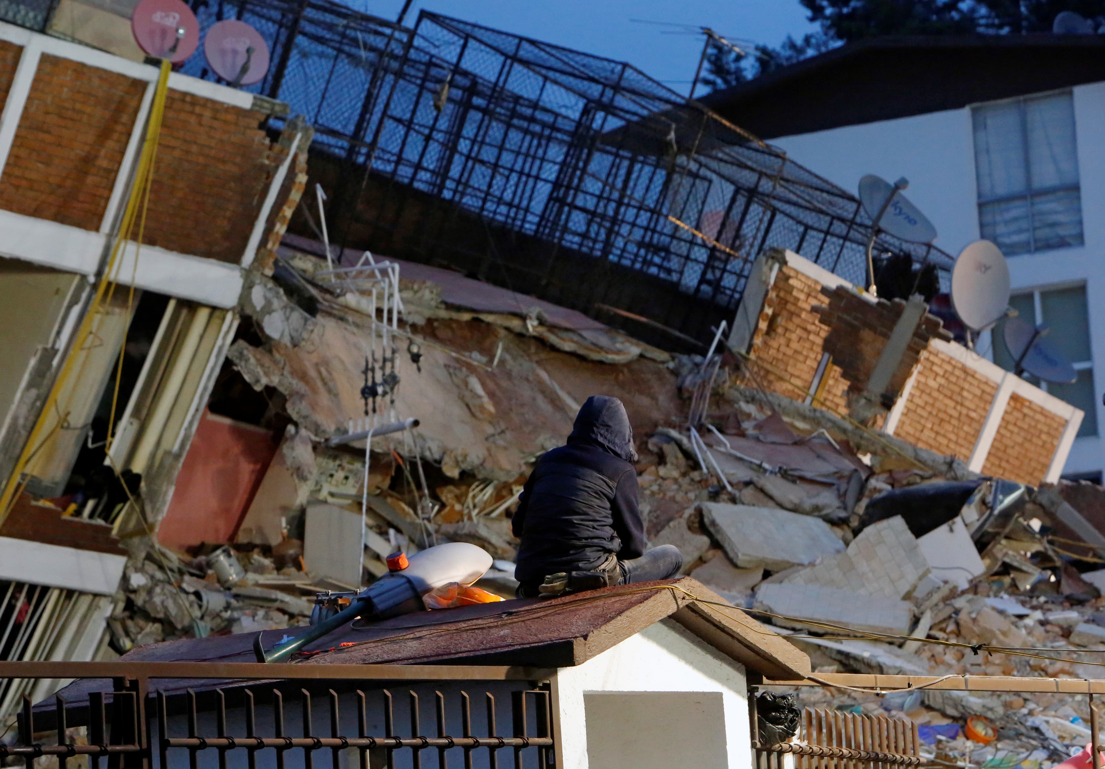 A person sits on the roof of a little house while looking at the rubble of a collapsed building after an earthquake hit Mexico City, Mexico September 20, 2017.