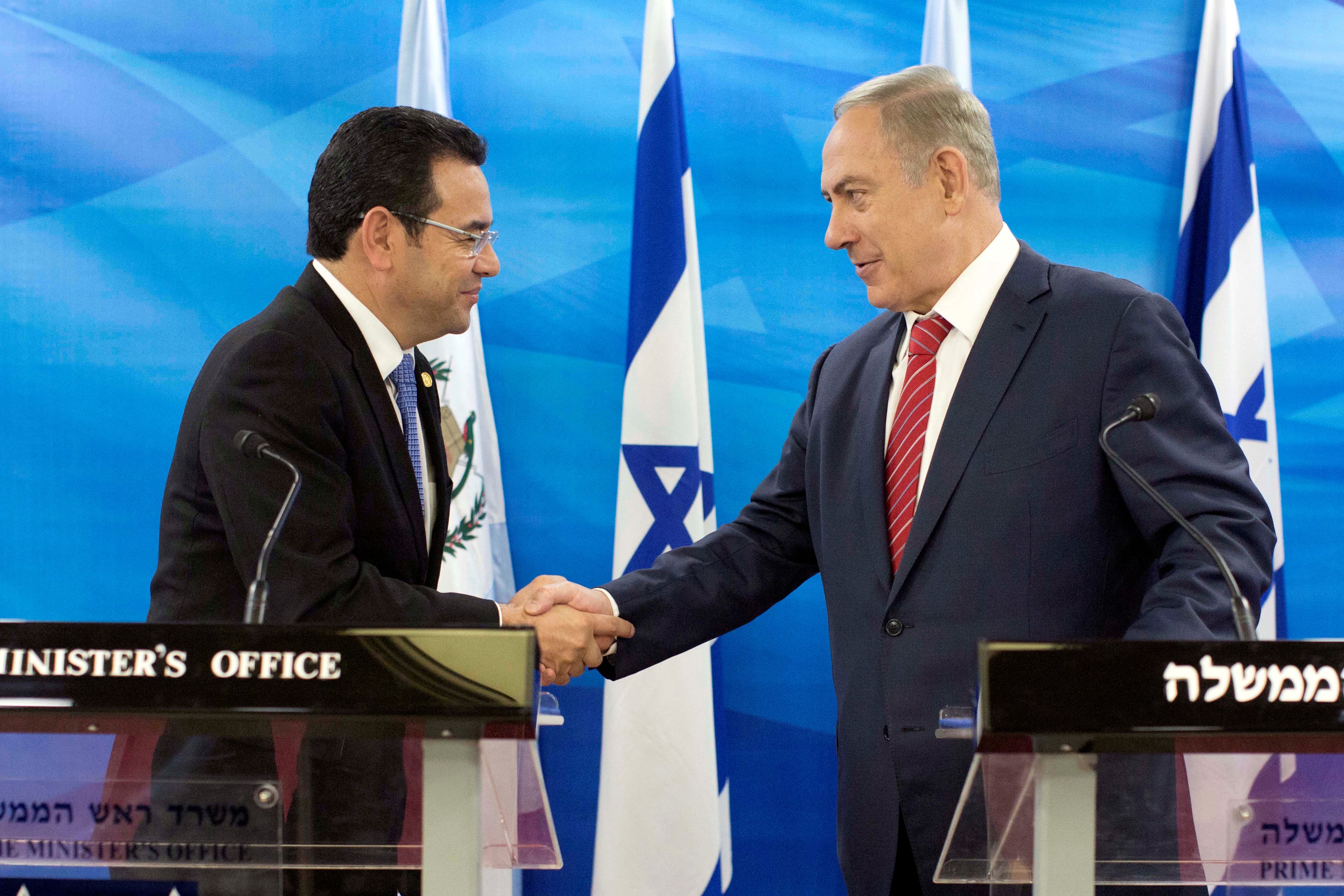 Two men shaking hands in front of flags