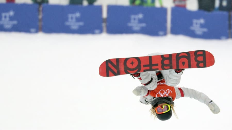 Woman on snowboard, in air, upside down in front of onlookers