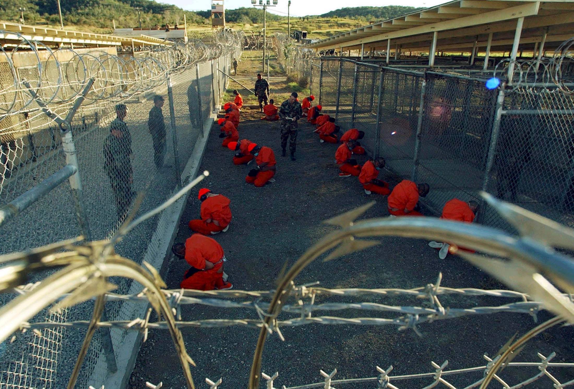 Detainees in orange jumpsuits sit in a holding area under the watchful eyes of military police during inprocessing at the temporary detention facility at Guantanamo Bay's Camp X-Ray in this January 11, 2002 file photograph.