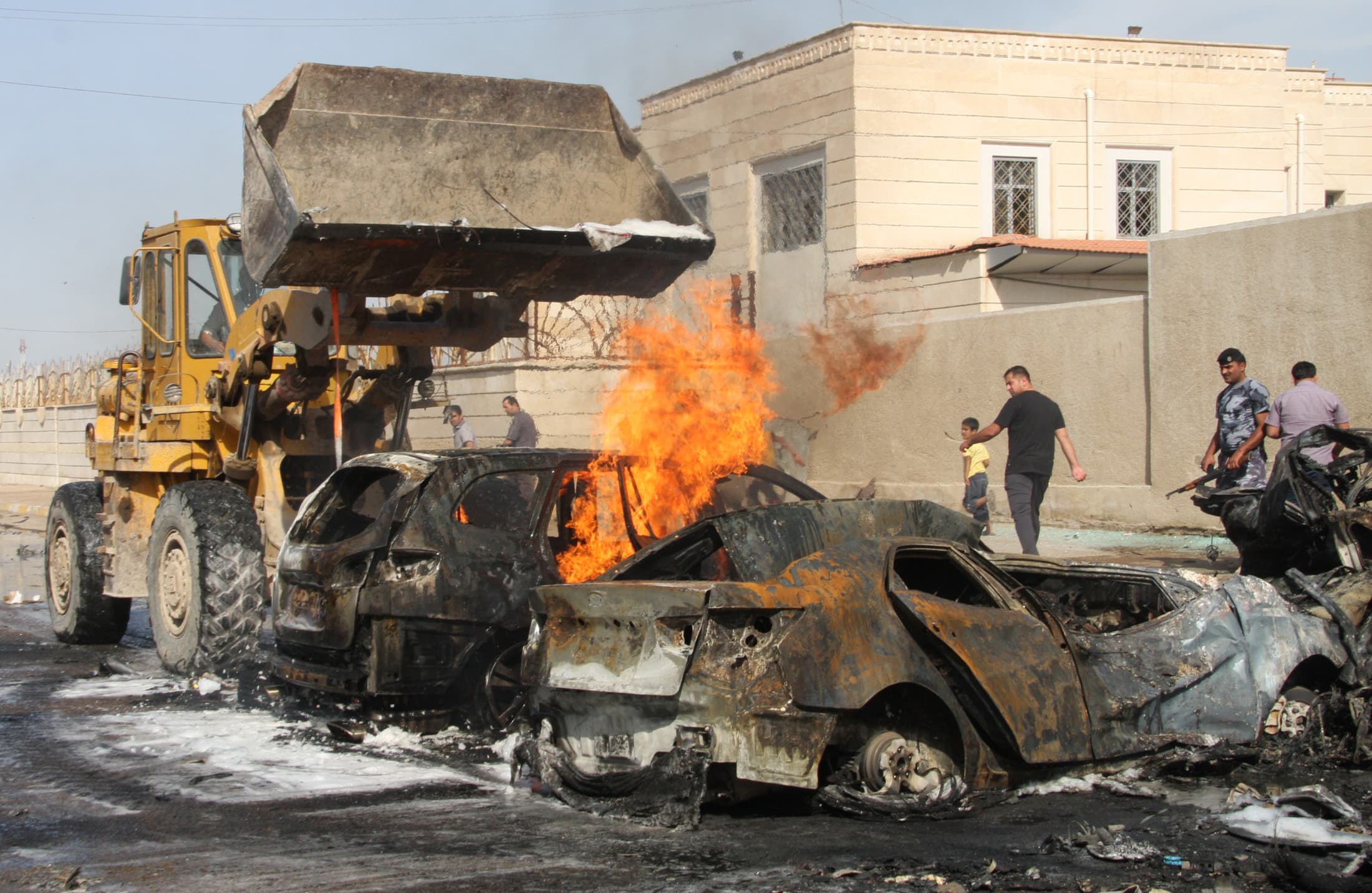 A bulldozer attempts to extinguish a fire in a destroyed vehicle at the site of a bomb attack in Baghdad.