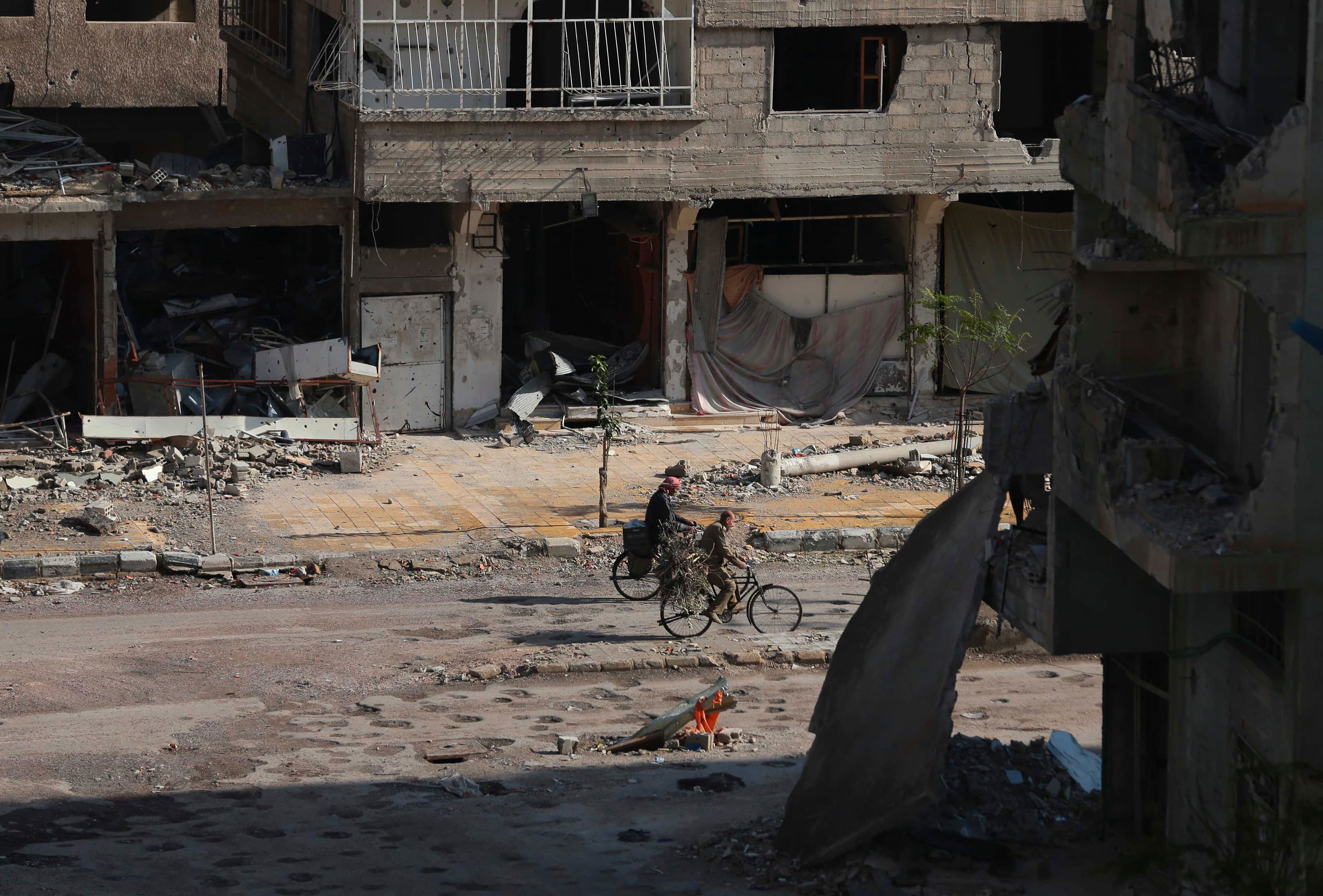 Men ride bicycles past damaged buildings along a street in the Duma neighborhood of Damascus, December 2013.