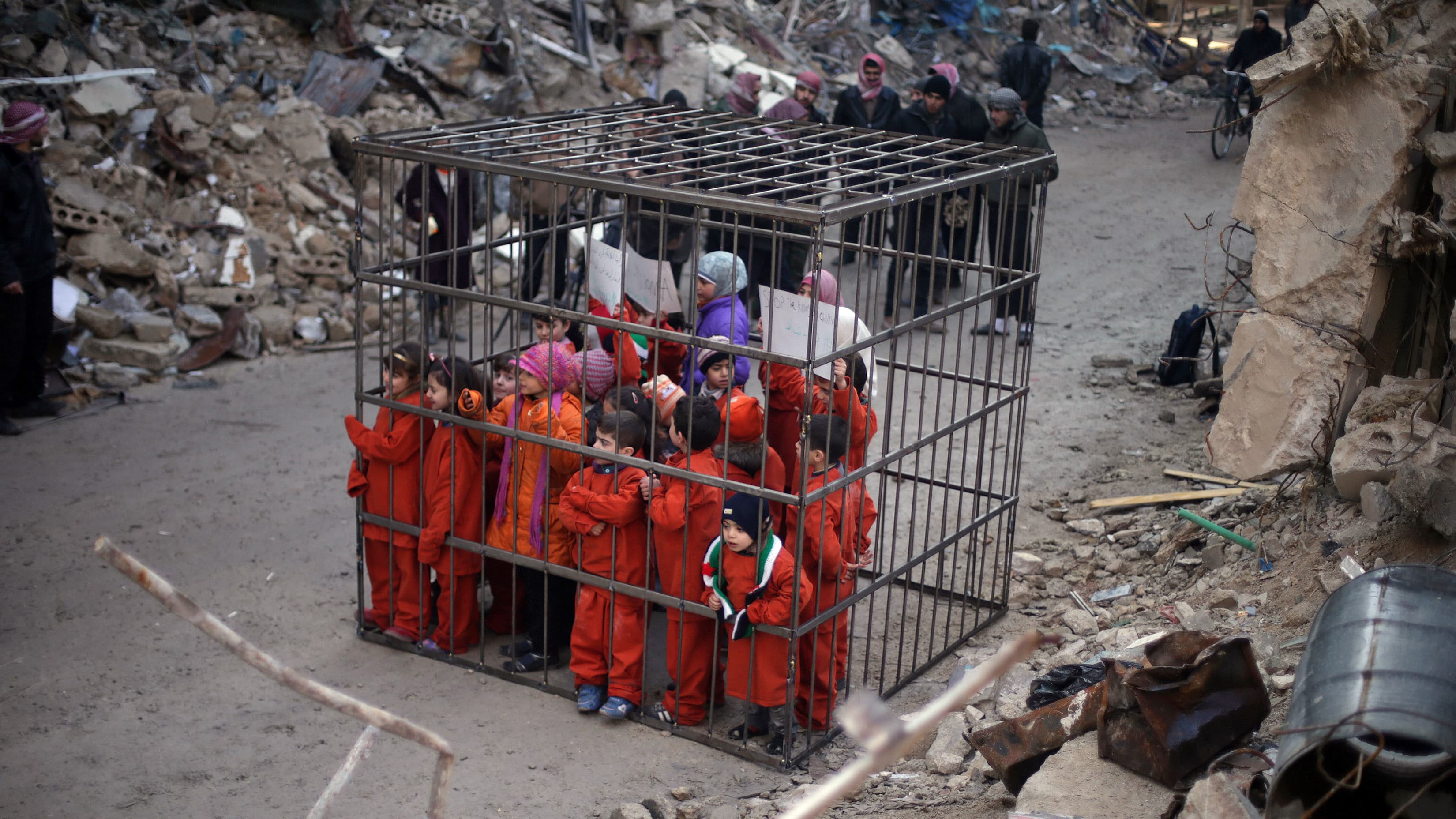 Children carry banners inside a cage during a protest against forces loyal to Syria's President Bashar al-Assad near Damascus, February 15, 2015.