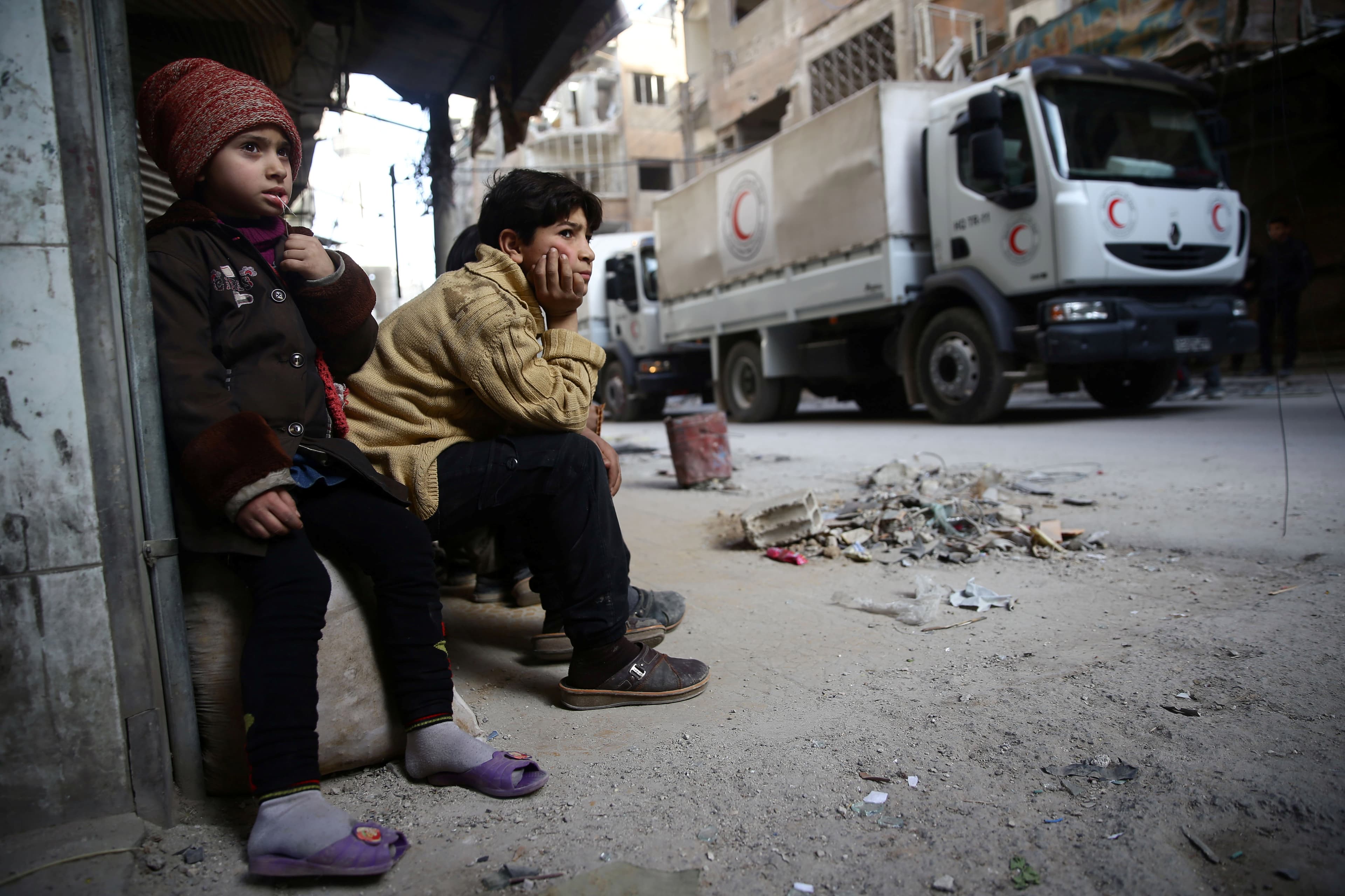 Children watch as an aid convoy of Syrian Arab Red Crescent drives through the besieged town of Douma, Eastern Ghouta, Damascus, Syria March 5, 2018.