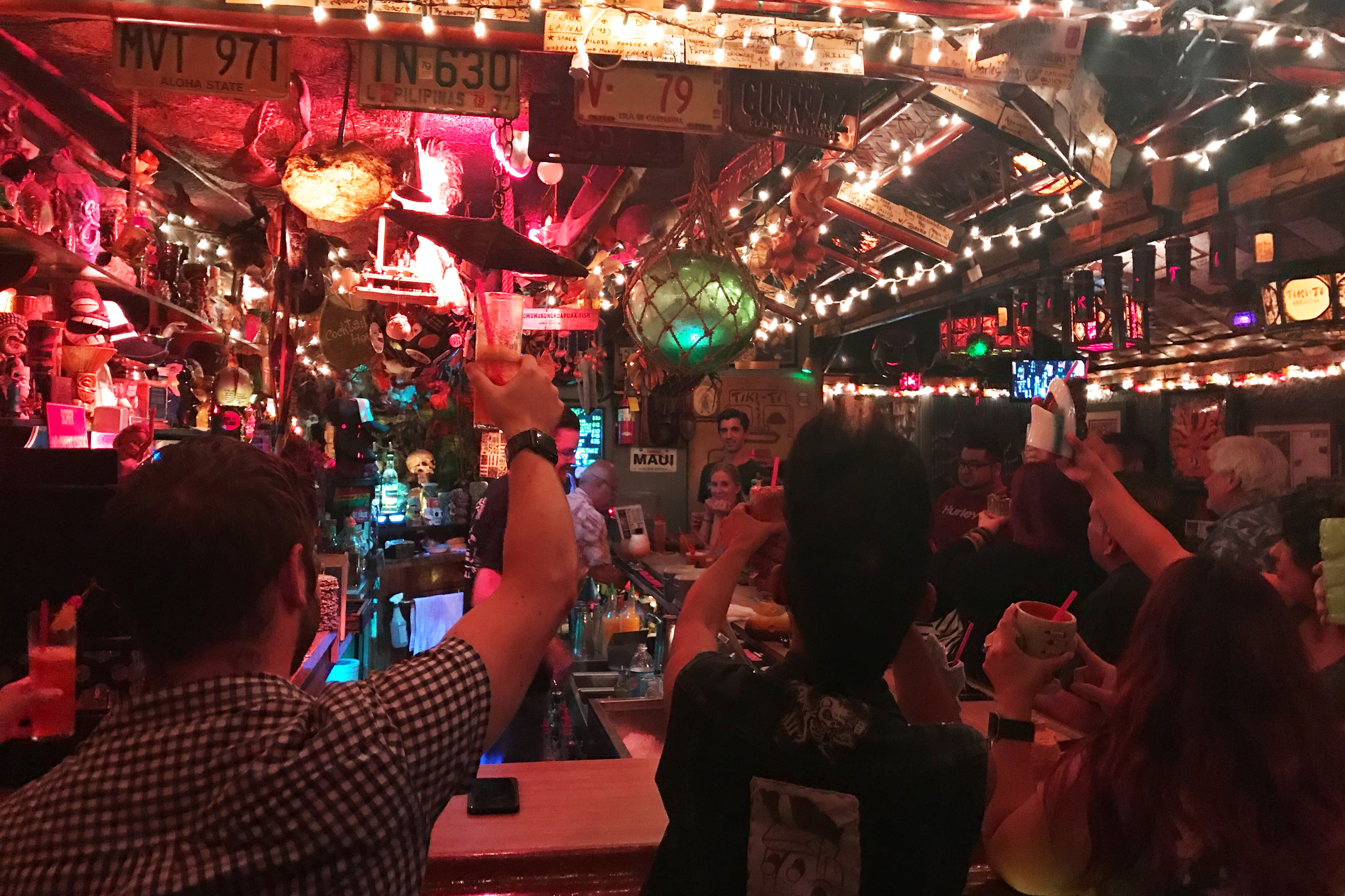Small and colorful bar with lights strung up, patrons raising their glass to the back wall
