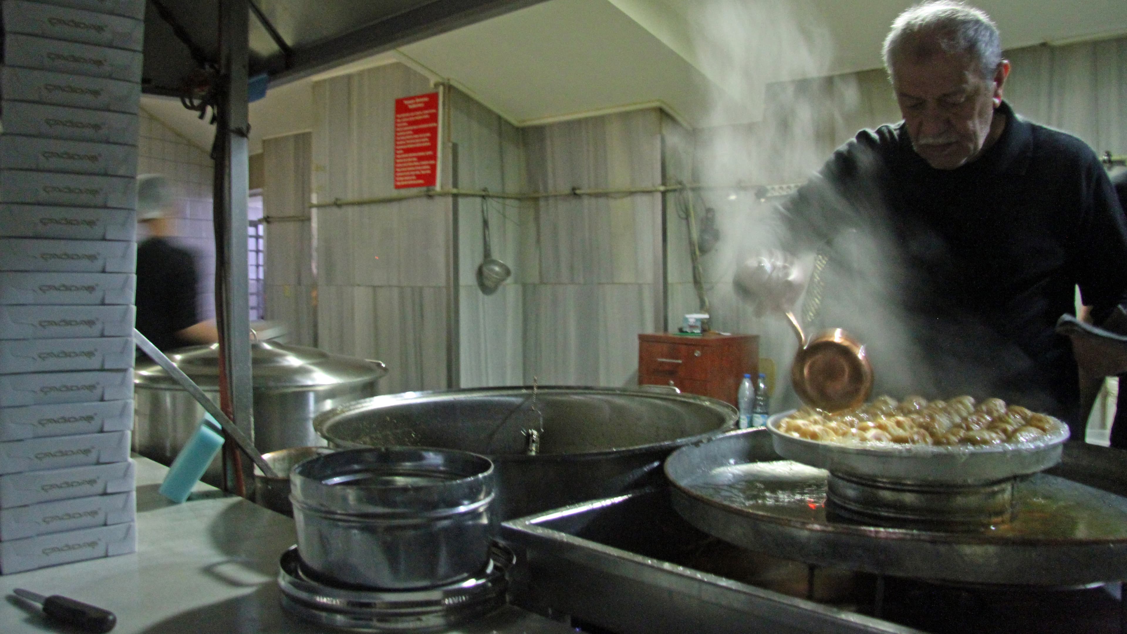 Talet Cagdas, the owner of Gaziantep's Imam Cagdas restaurant, pours a sugary melted butter mixture over one of the day's first batches of Baklava. It's the finishing touch on a labor intensive sweet.