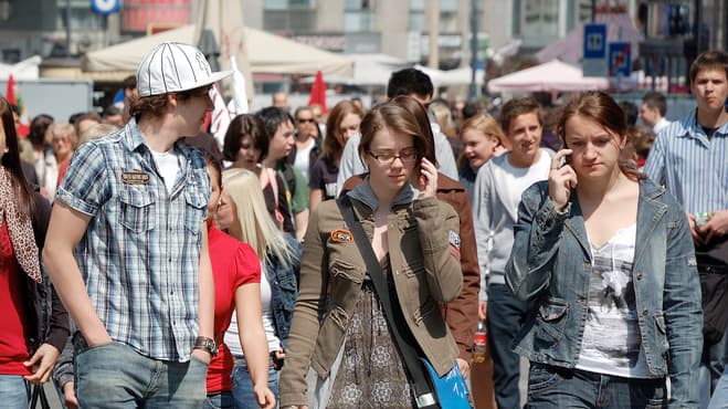 Two young women walk down a street while talking on the phone.