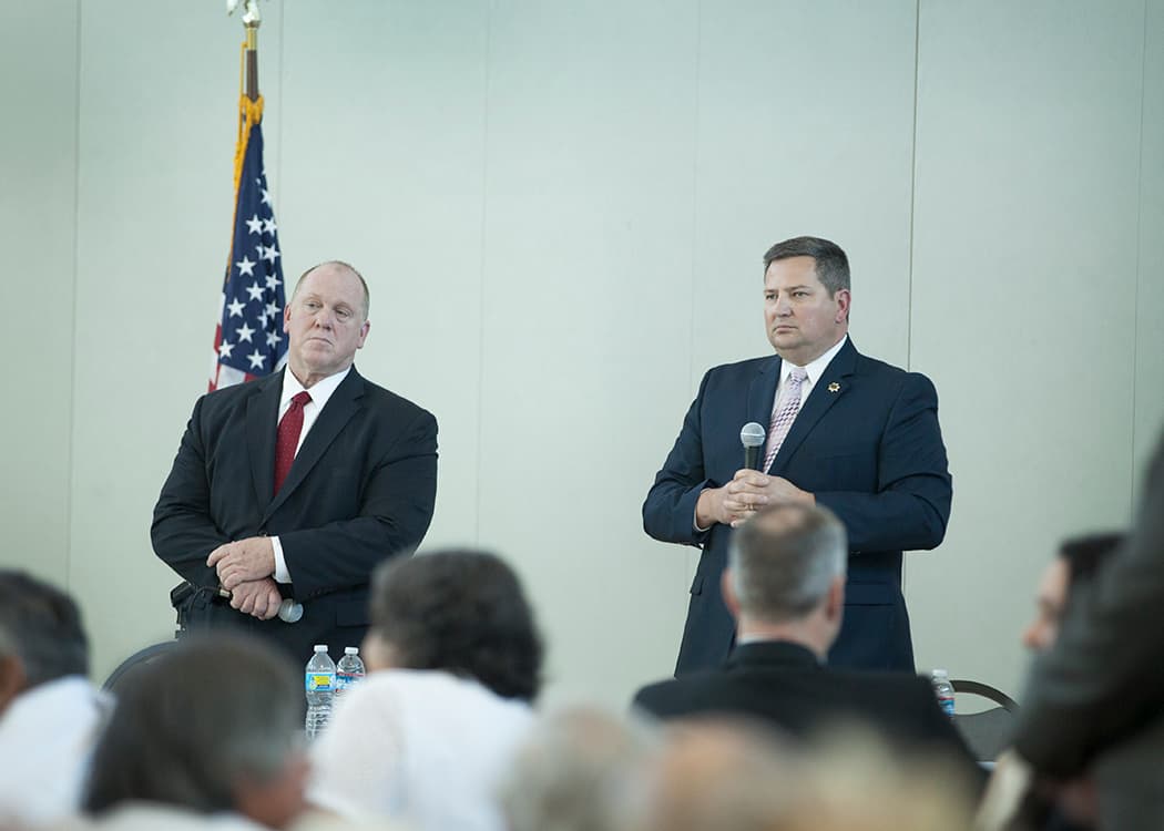 Two men in suits at front of room holding microphones
