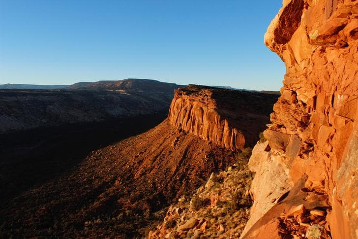 The craggy ridge of a formation of red rocks is pictured under a cloudless blue sky in Utah.