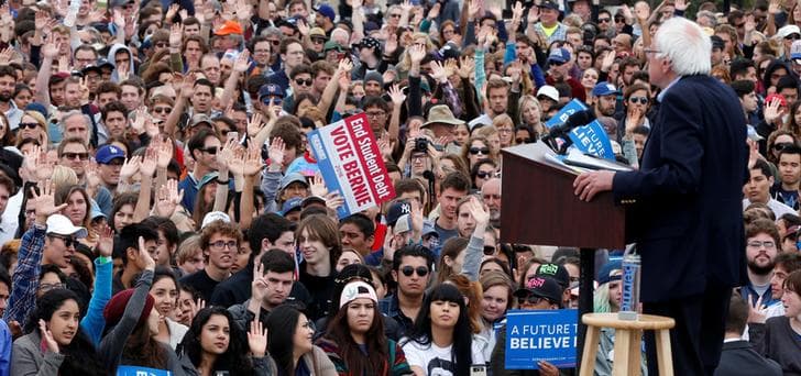 Democratic presidential candidate Bernie Sanders faces a very large crowd of young people who hold their hands up in the air after he asks who among them has student loans.