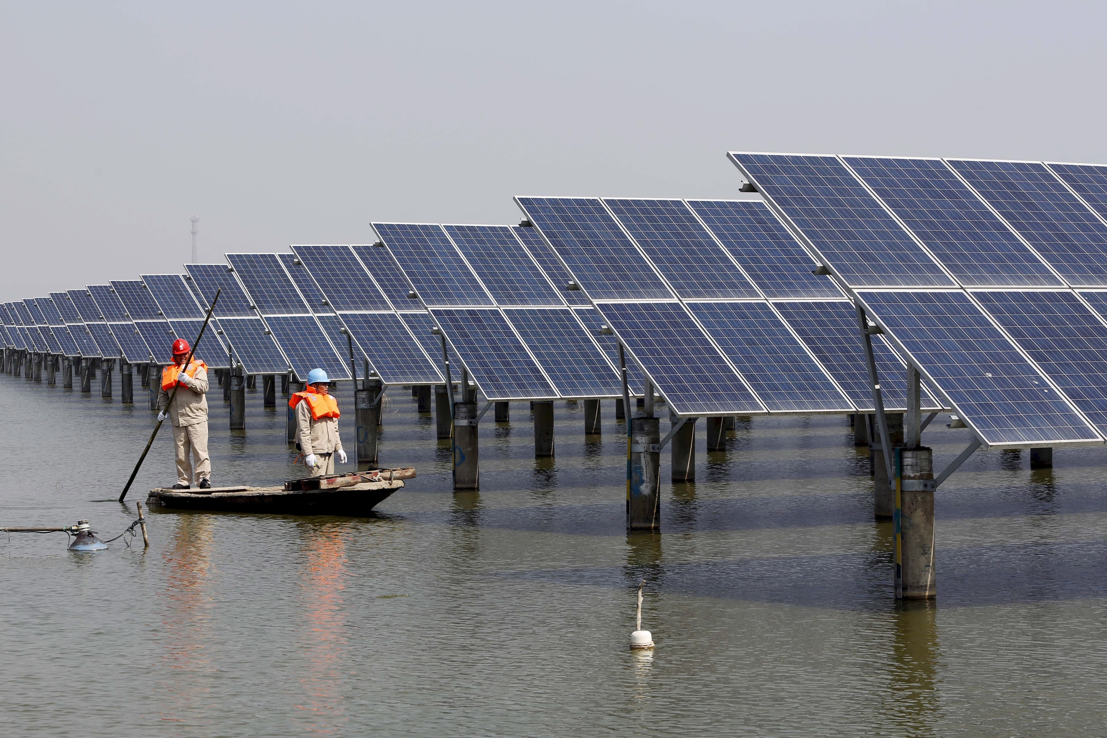 Employees row a boat as they examine solar panel boards at a pond in Lianyungang, Jiangsu Province, China, in this March 16, 2016 photo.