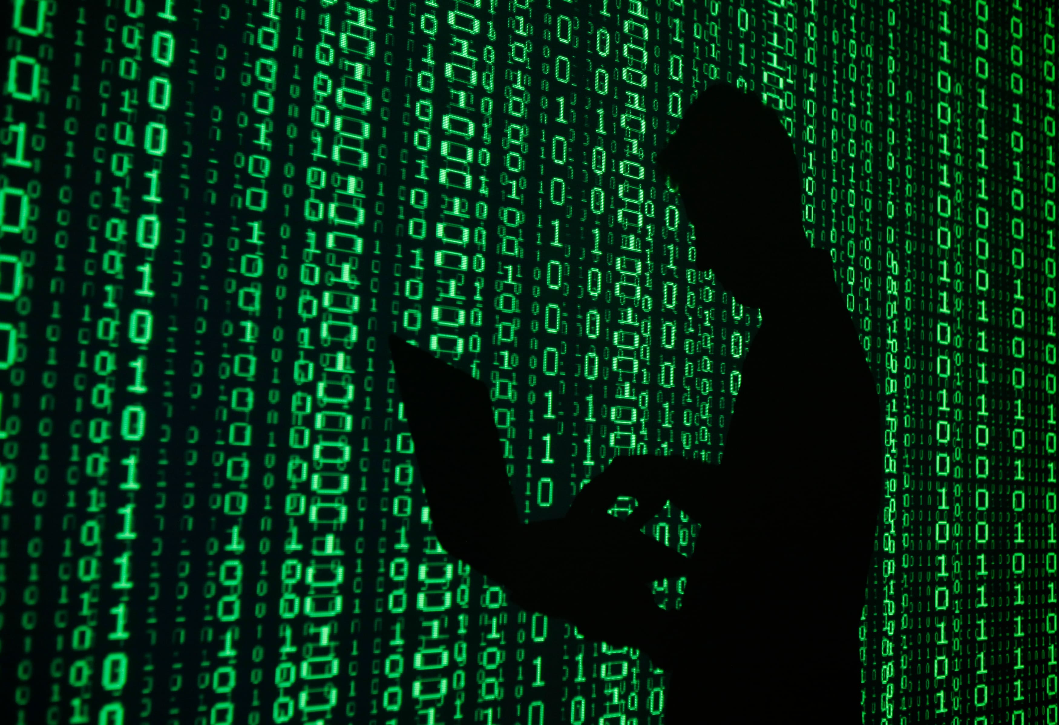 An illustration shows a projection of binary code around the shadow of a man holding a laptop computer in an office in Warsaw June 24, 2013.