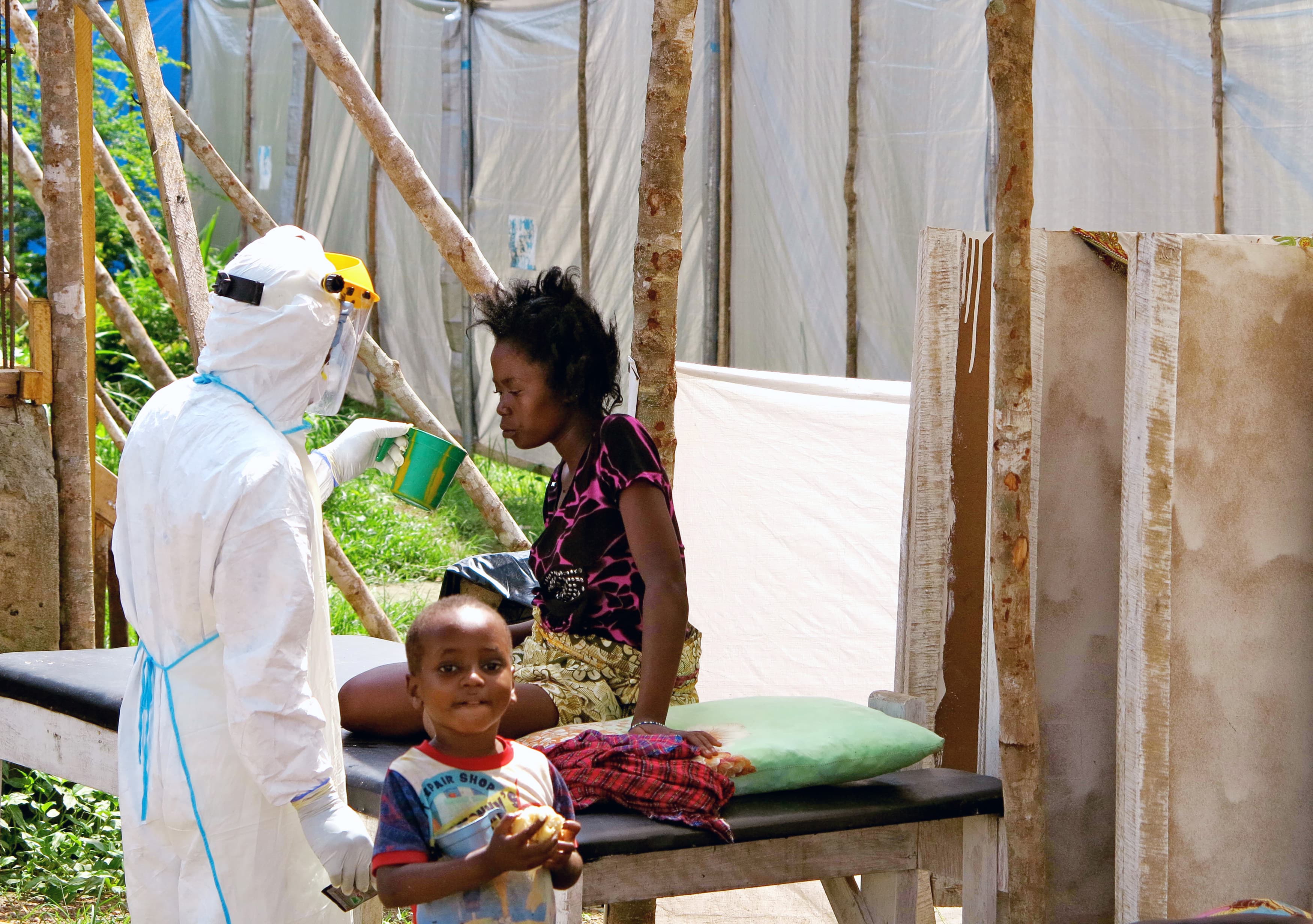 A health worker, wearing head-to-toe protective gear, offers water to a woman with Ebola at a treatment center for infected persons at Kenema Government Hospital in Kenema, Sierra Leone.