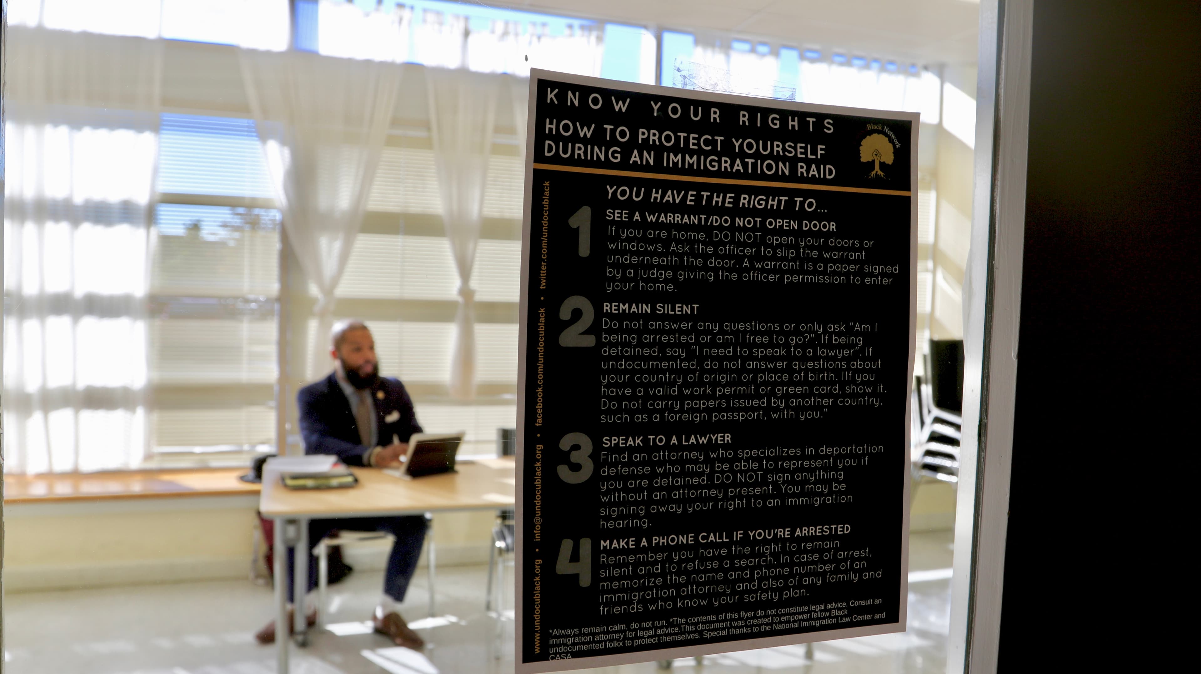 Window with poster about how to handle immigration raids, man behind at table