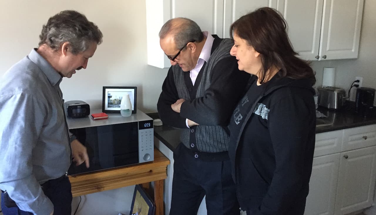 Jim Estil stands with a Syrian couple he's helped resettle in Guelf, Canada. They're pointing out the Danby Applicances logo on their microwave; Estil runs the Danby factory and the couple works there.