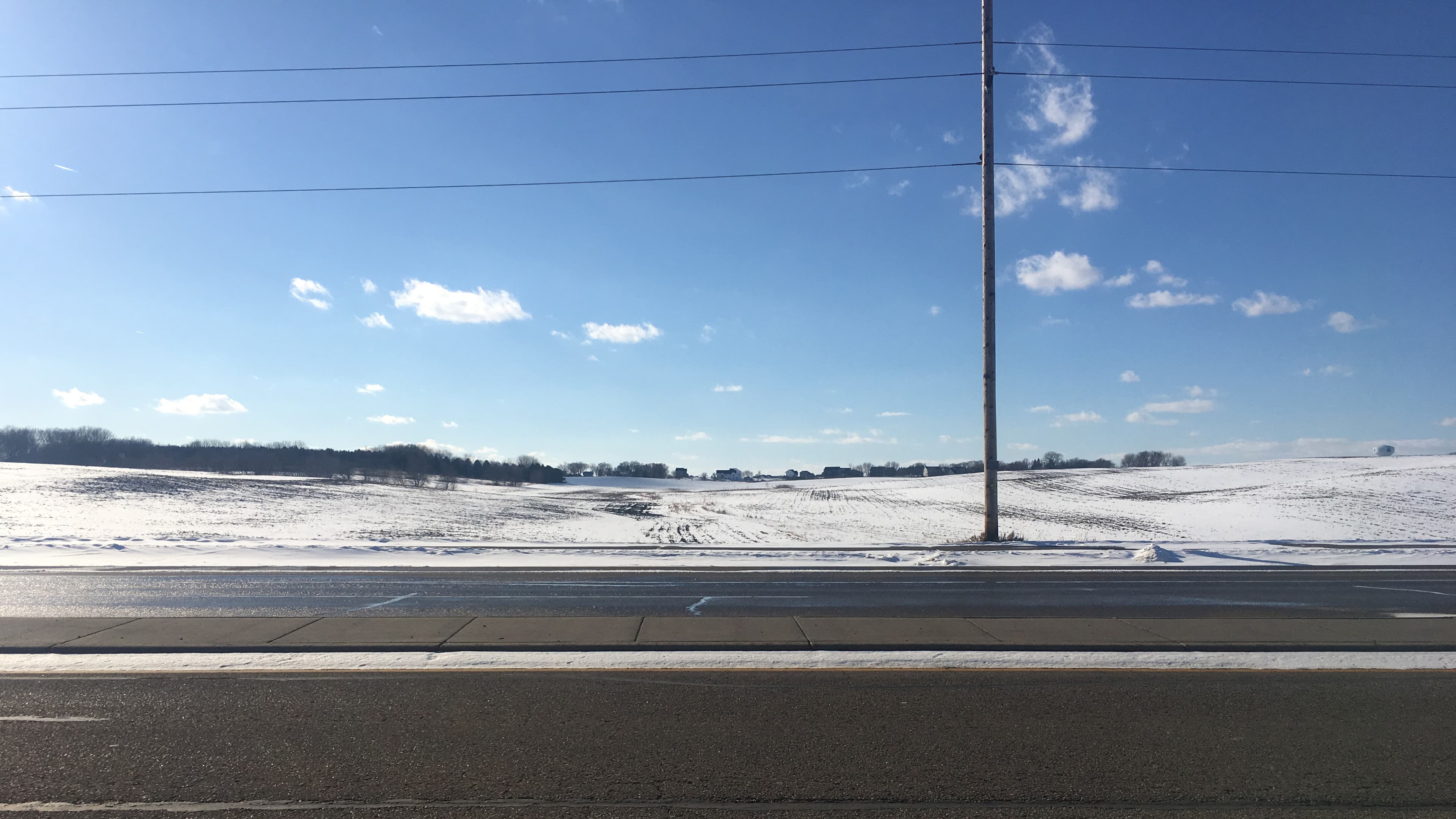 Sunshine on an empty road with snow-covered farmland in the background