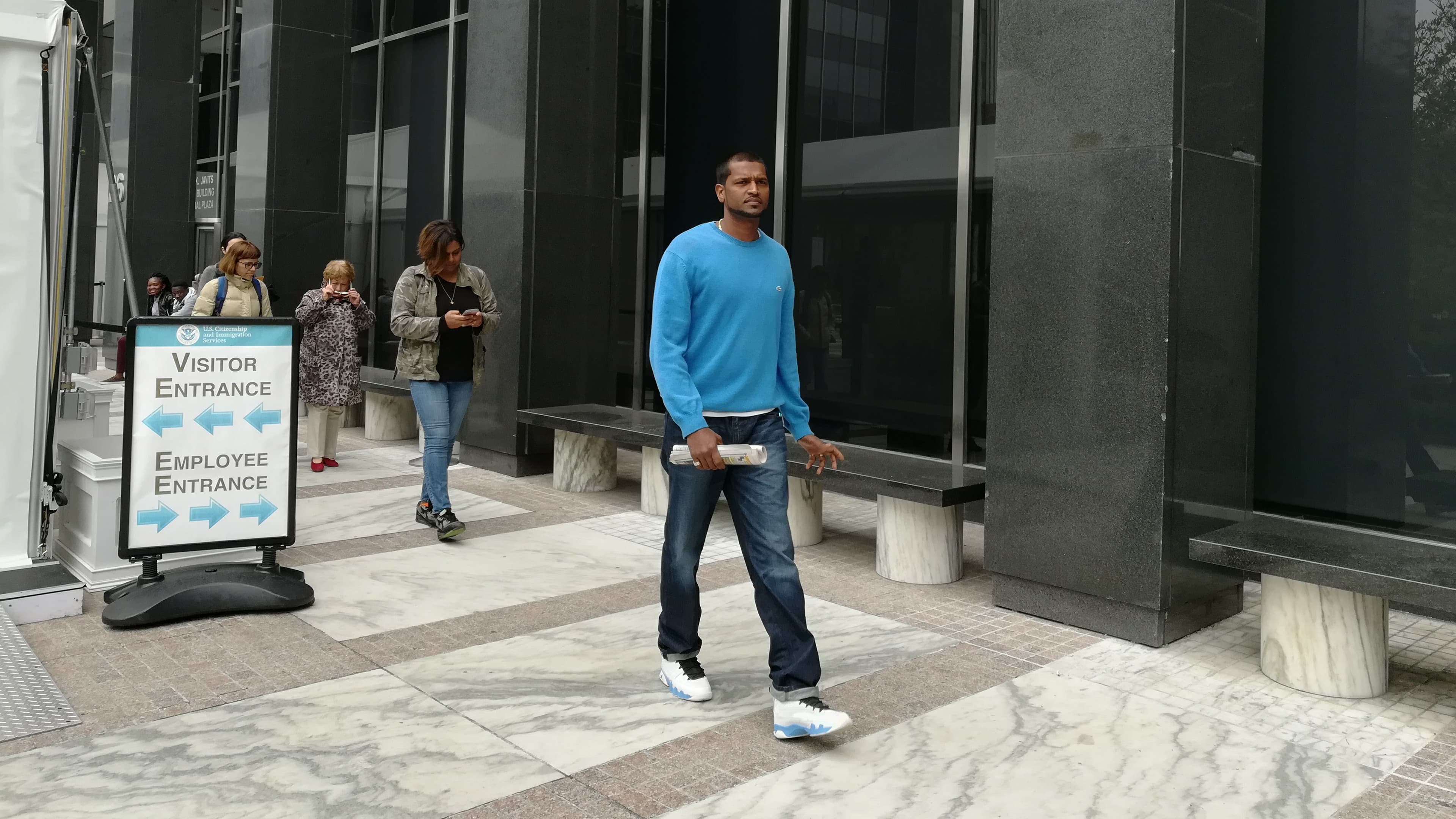 Man walks out of building with sign of immigration agency behind him