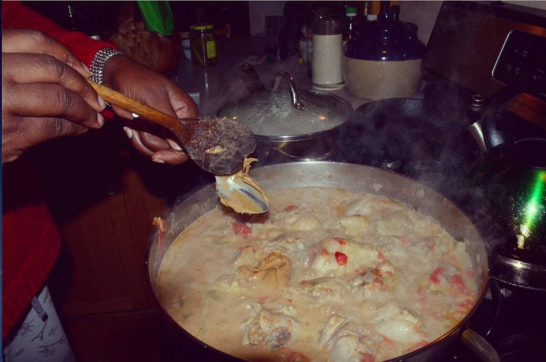 A dish on the stove with a woman's hands and a spoon adding peanut butter