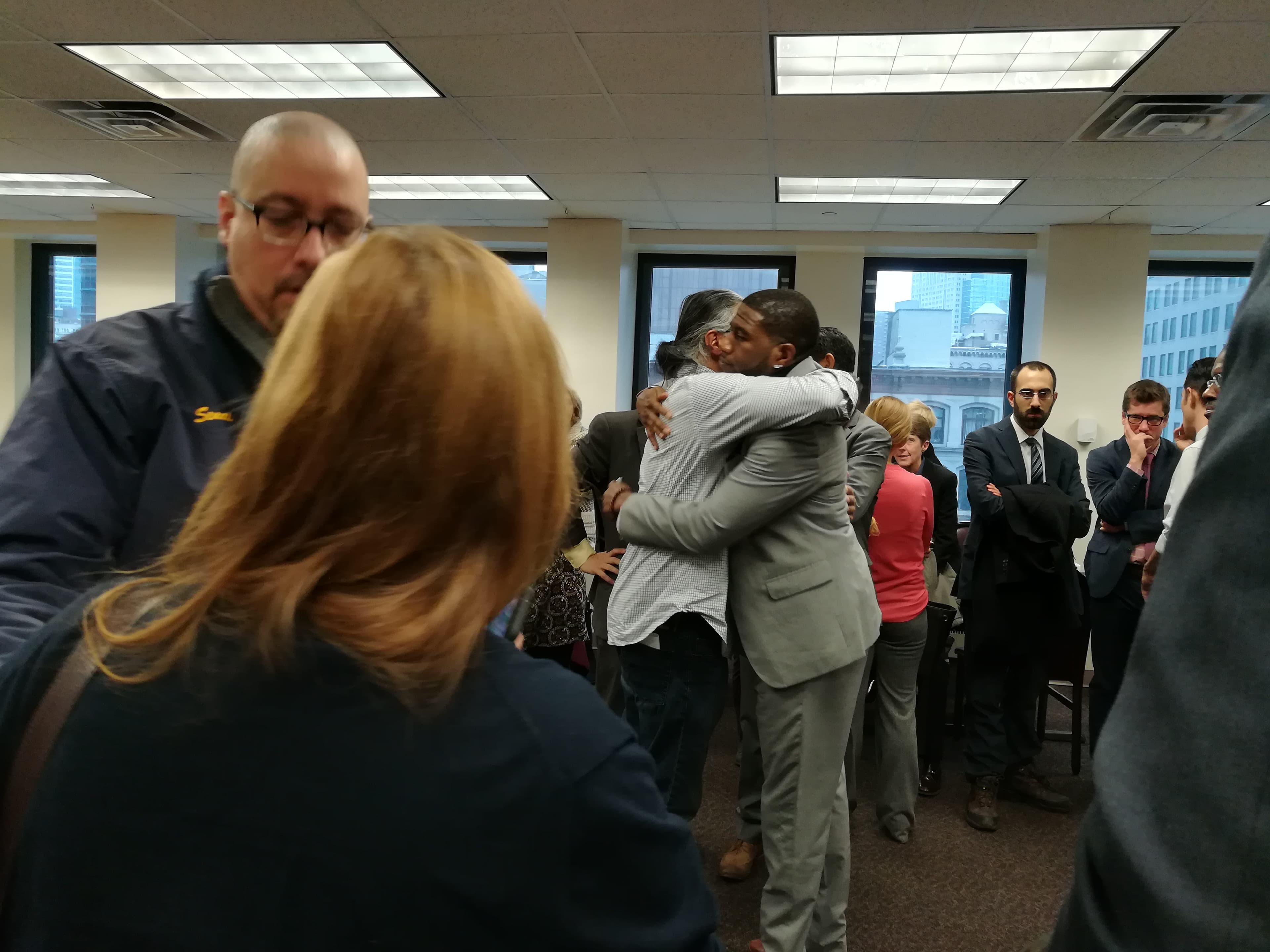 Two men hug in room with many people around them