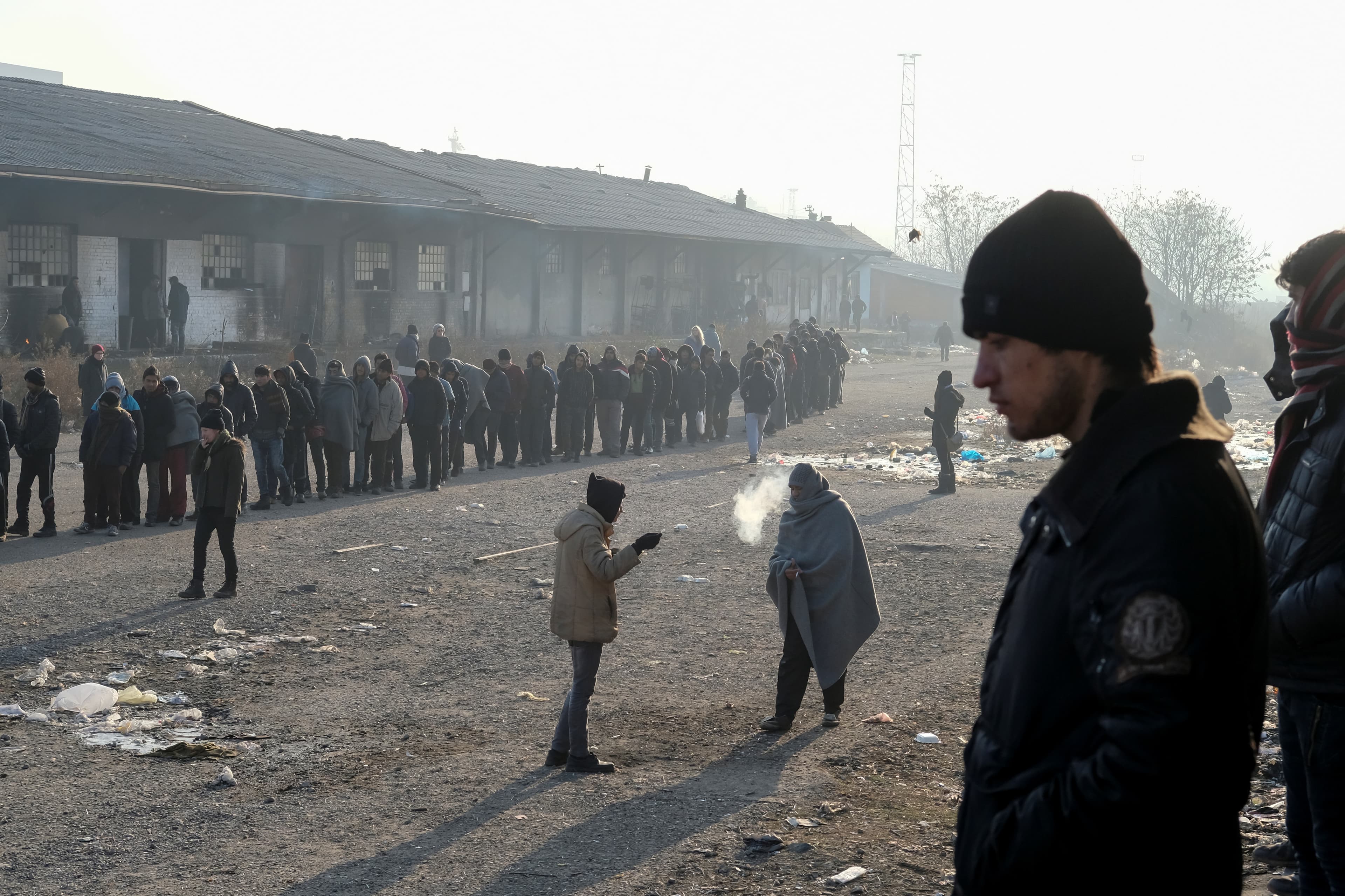 Migrants stand in line to receive free food outside a derelict customs warehouse in Belgrade