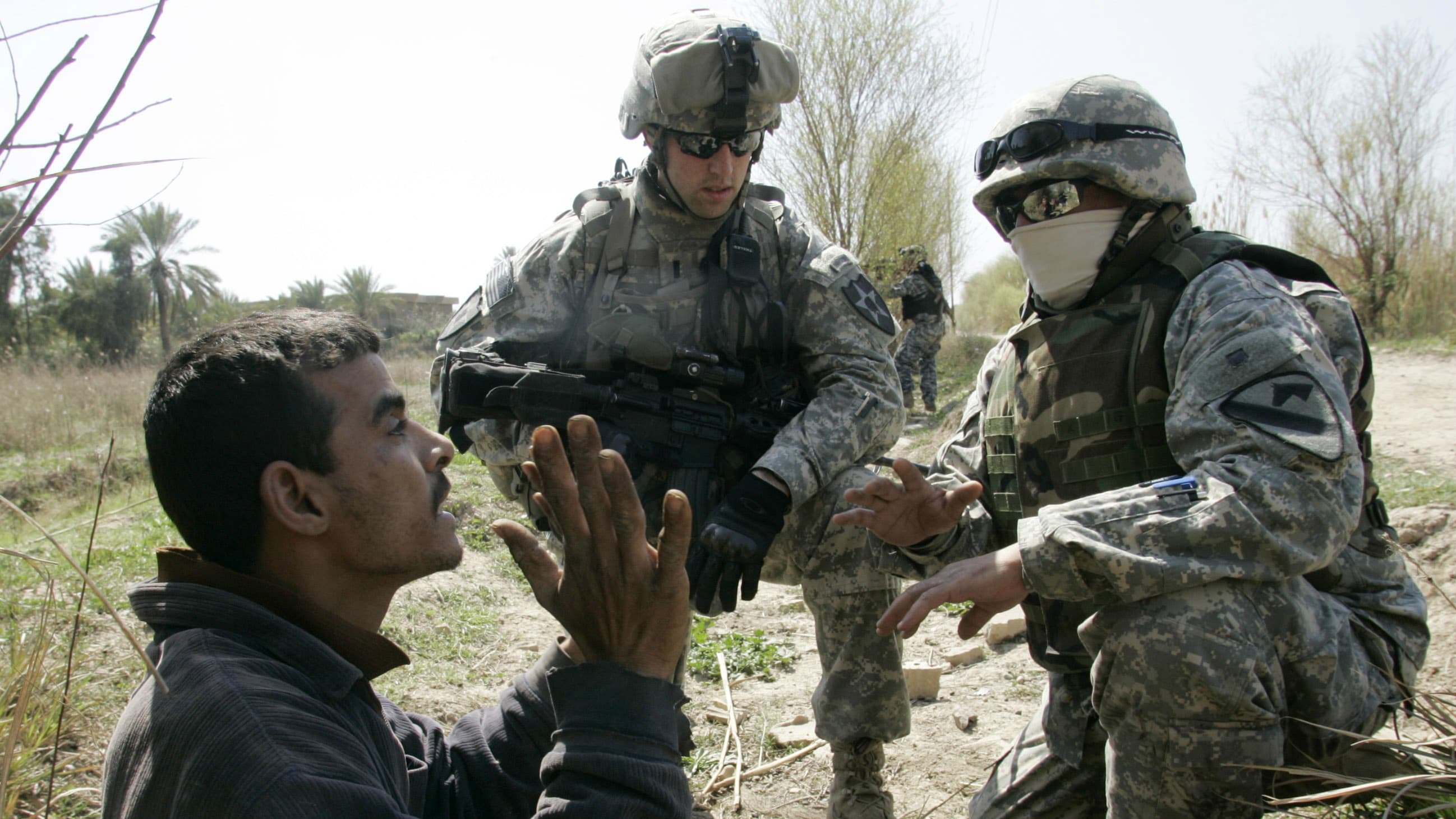 A US soldier of the 2nd Platoon Charlie Troop, 3rd Squadron of 61st Cavalry Regiment questions a man with an interpreter (R) while on patrol with Iraqi National Police in a suburb of Baghdad, March 7, 2007.
