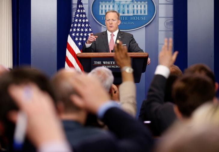 White House Press Secretary Sean Spicer points to a reporter during a press conference as several hands rise up from the crowd of questioning journalists.