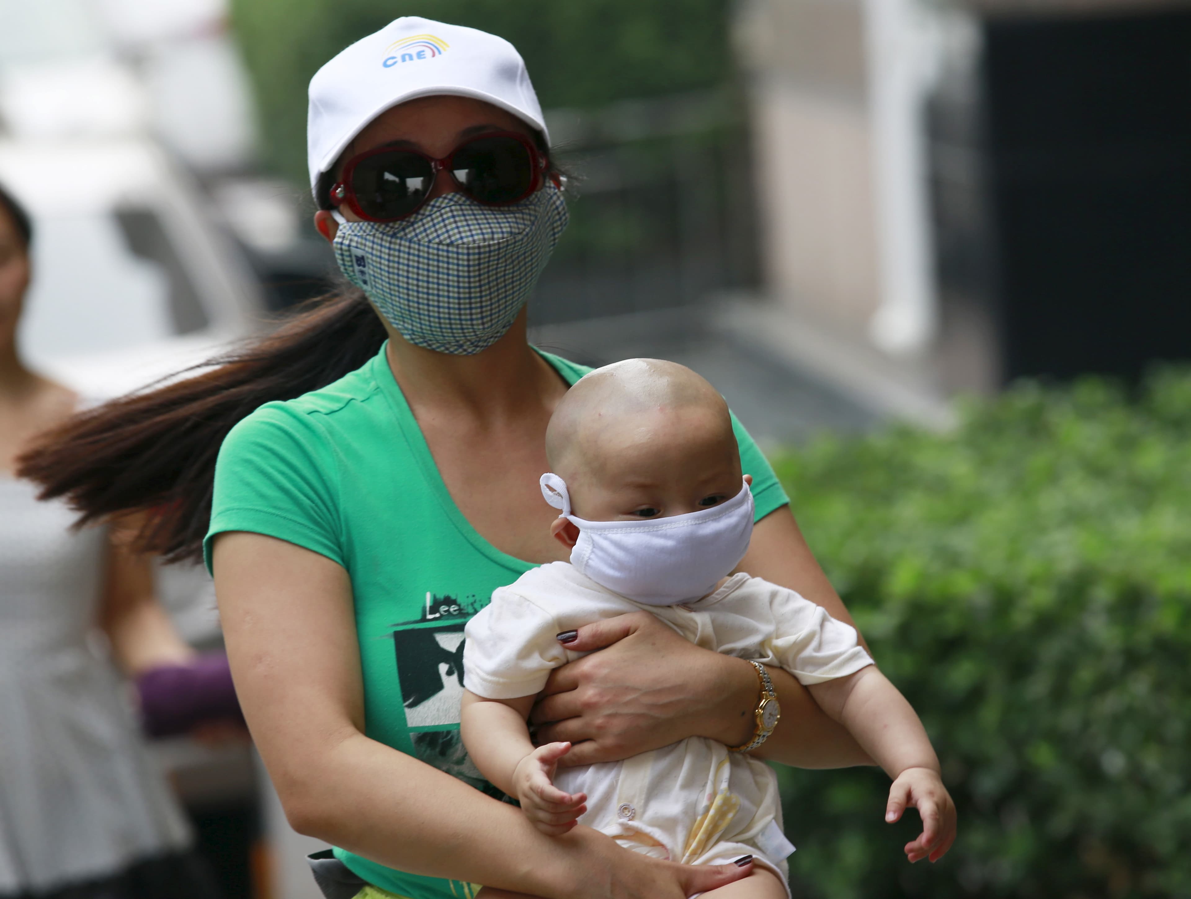 A woman carrying a baby, both wearing masks, make their way down a street and away from the site of explosions, in Tianjin, China.