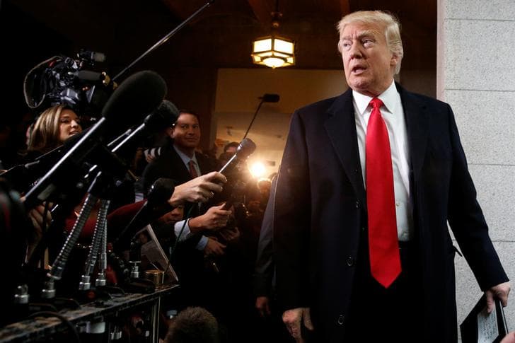 President Donald Trump (r) looks toward a crowd of reporters who hold microphones and point cameras in his direction.
